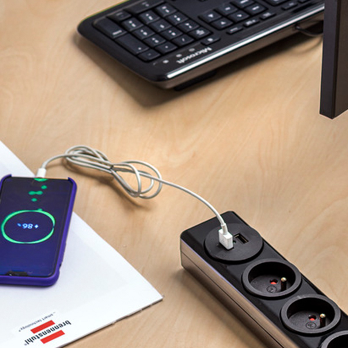 Ein Smartphone wird an eine schwarze Steckdosenleiste mit USB-Anschluss geladen.