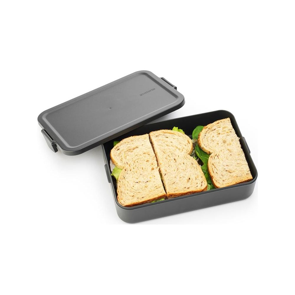 Un contenitore grigio per il pranzo con coperchio, riempito con quattro mezze fette di sandwich con lattuga.