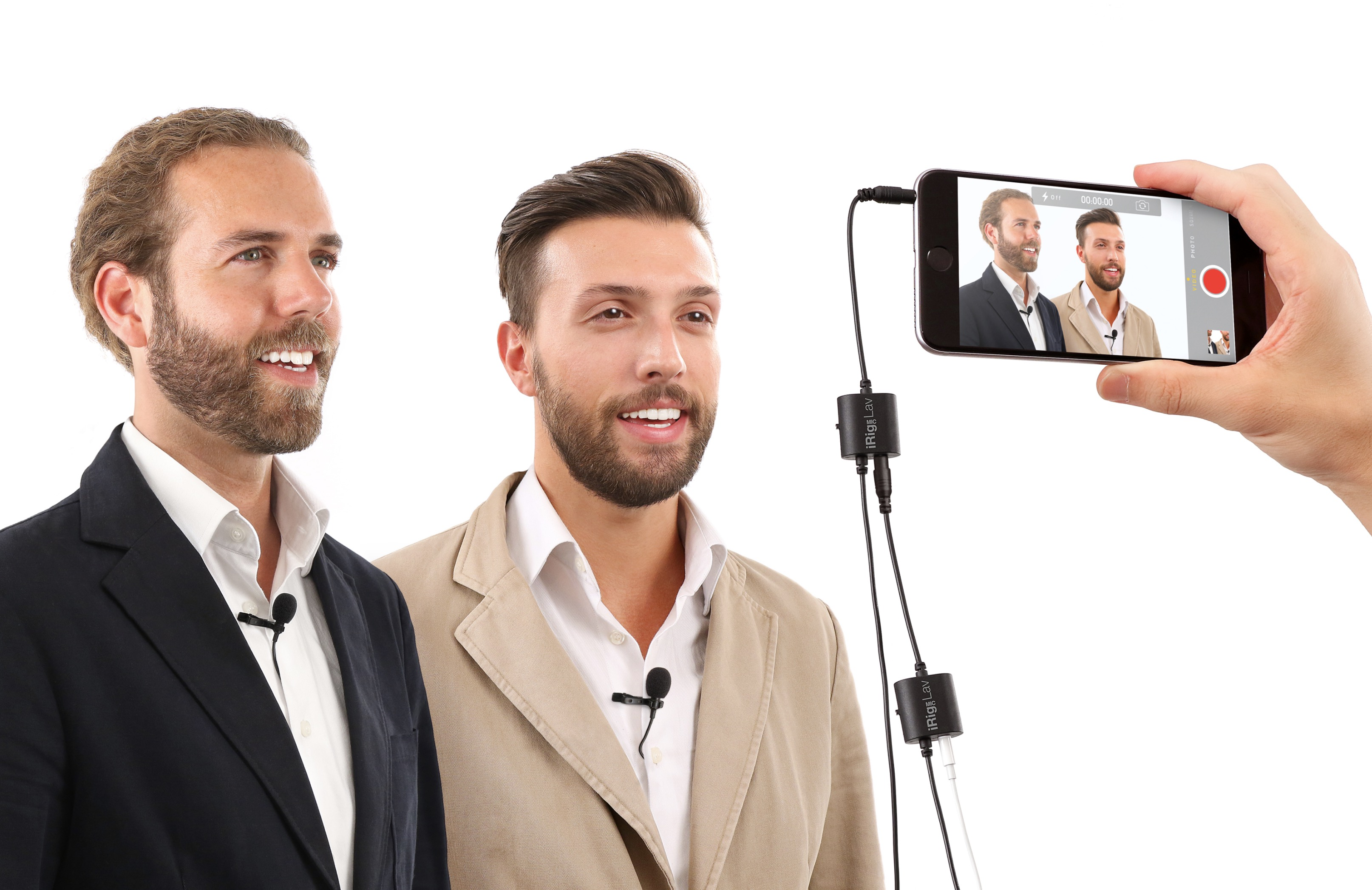 Due uomini con microfoni, una mano tiene uno smartphone che li riprende.