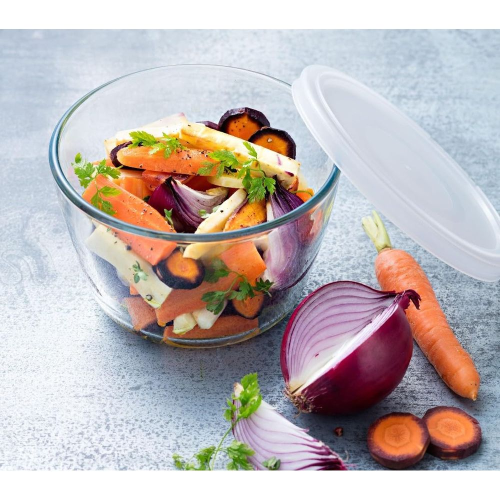 Ciotola di vetro con verdure a radice preparate, cipolle e carote accanto.