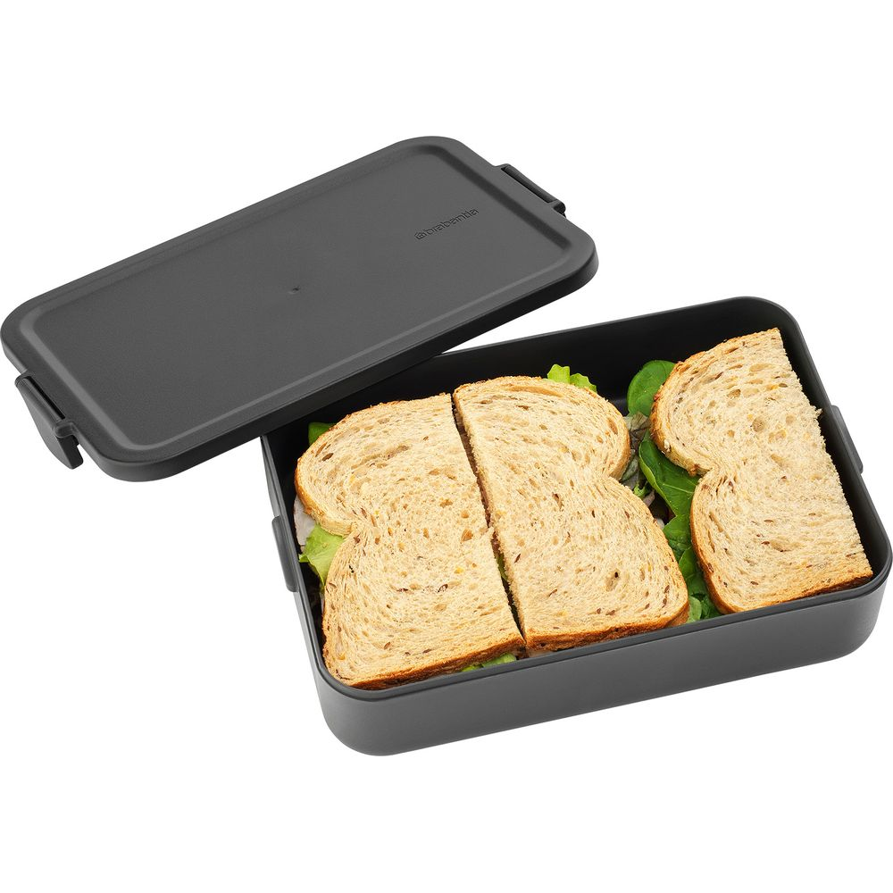 Un portapranzo grigio scuro con panini integrali e lattuga all'interno.
