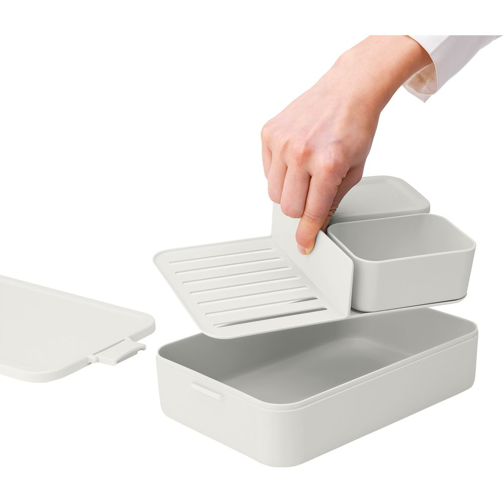 Una mano inserisce un inserto bianco a doghe in un contenitore rettangolare grigio.