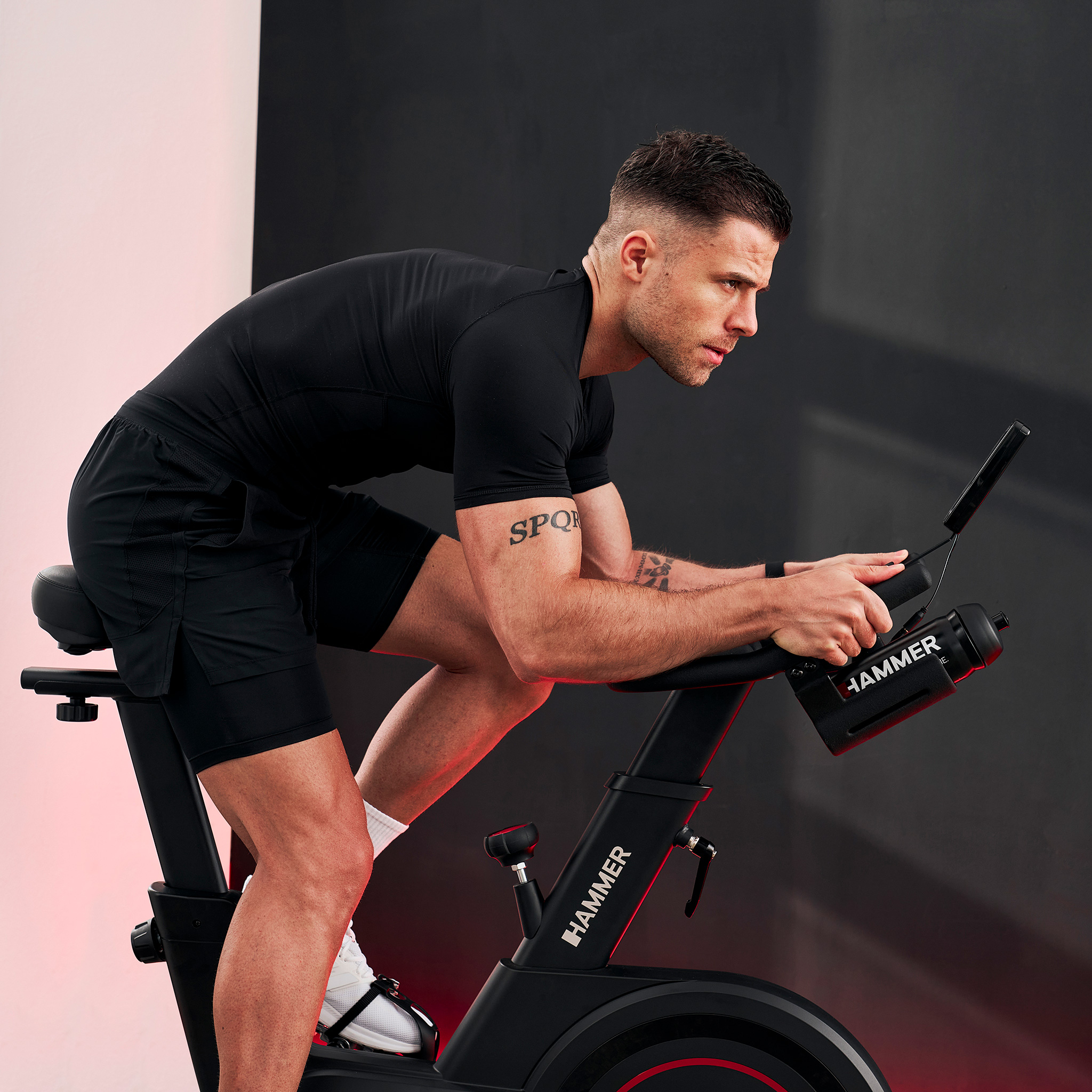 Mężczyzna na czarnym rowerze stacjonarnym z czerwonym oświetleniem w tle.