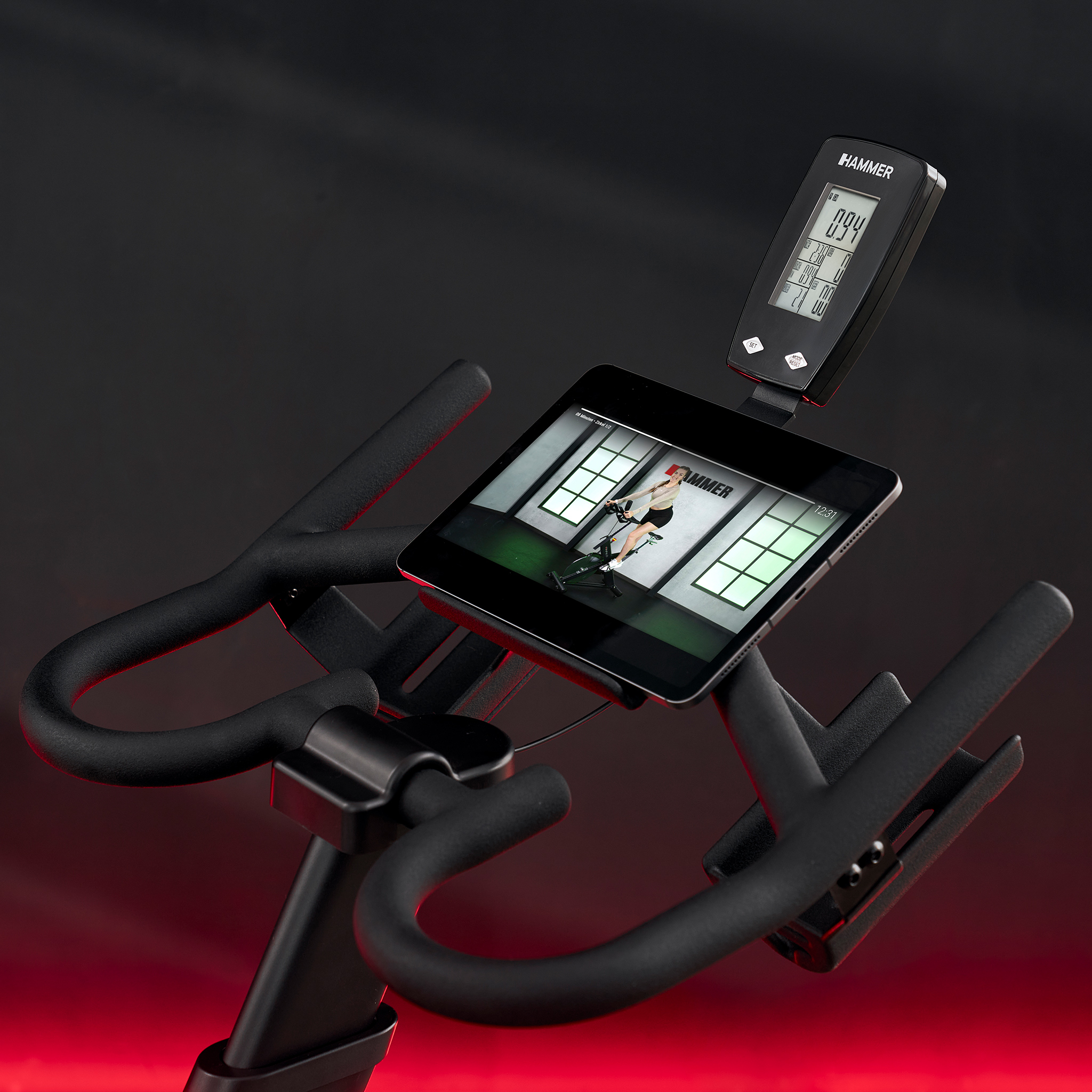 Czarny rower stacjonarny z tabletem pokazującym kobietę podczas jazdy.