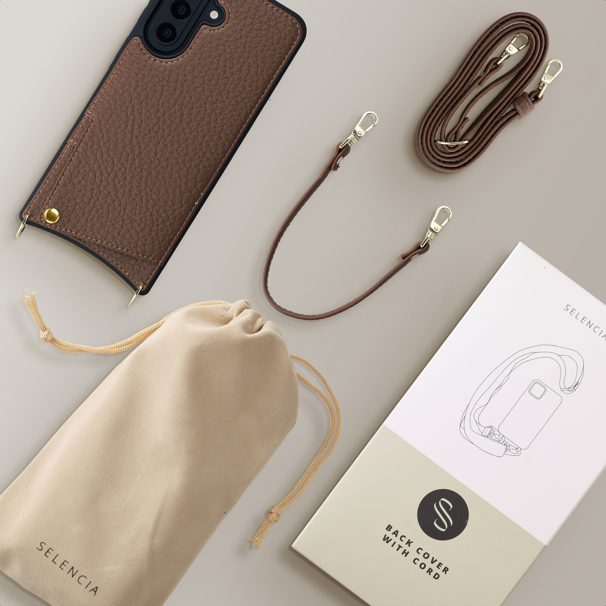 Étui en cuir marron, pochette et cordon avec quincaillerie dorée sur fond gris.