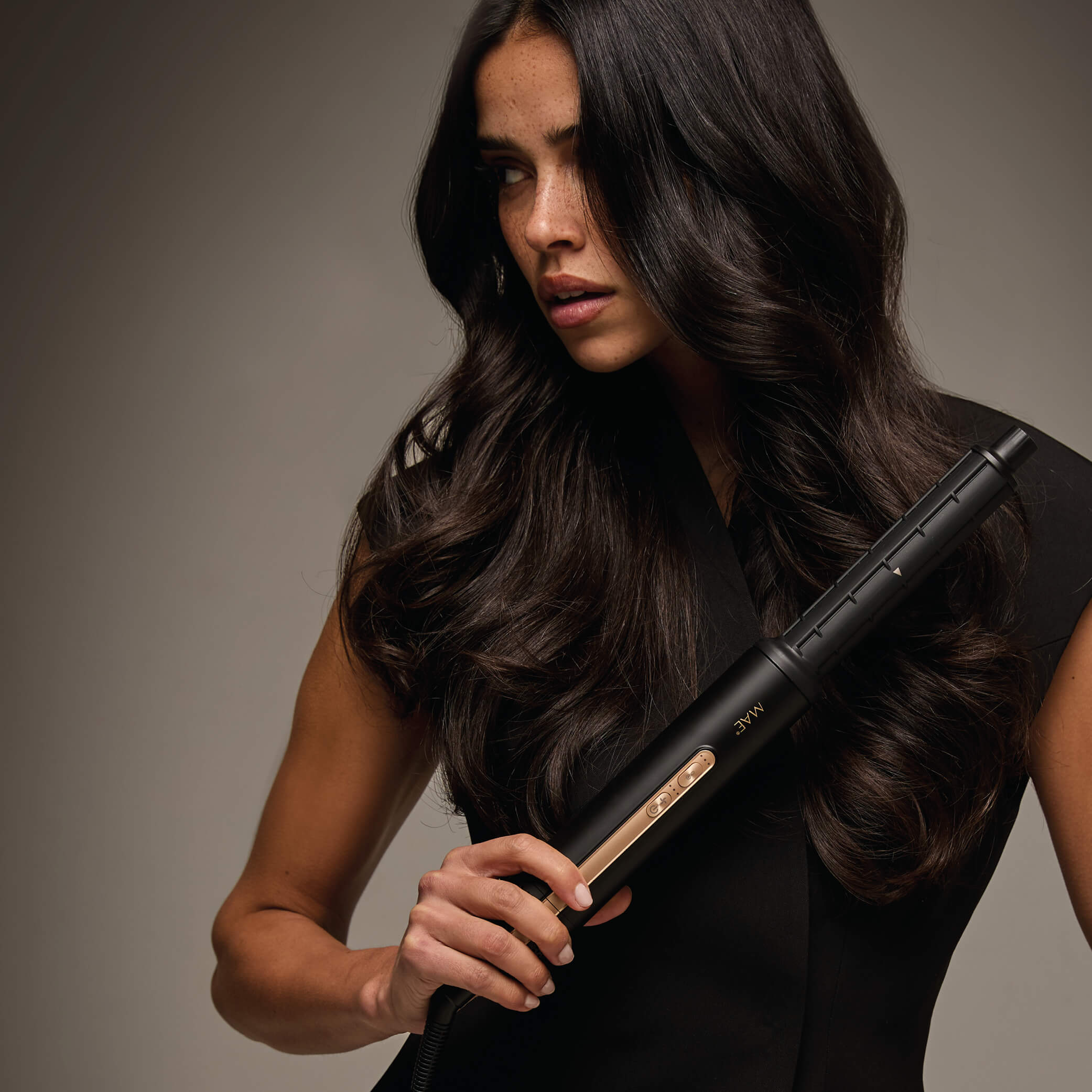 Een vrouw met lang donker haar houdt een zwarte haarstyler met gouden accenten vast.