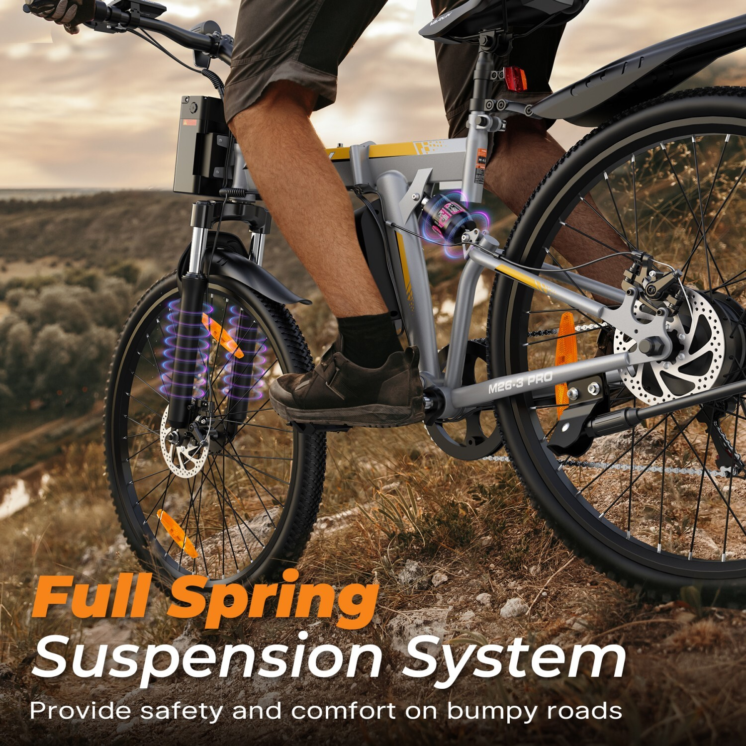 Osoba jedzie szarym rowerem elektrycznym z pełnym zawieszeniem sprężynowym po polnej drodze.