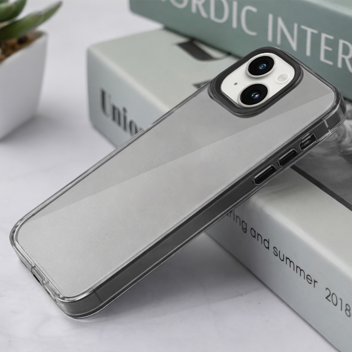 Une coque de téléphone transparente à bordure gris foncé repose sur des livres.