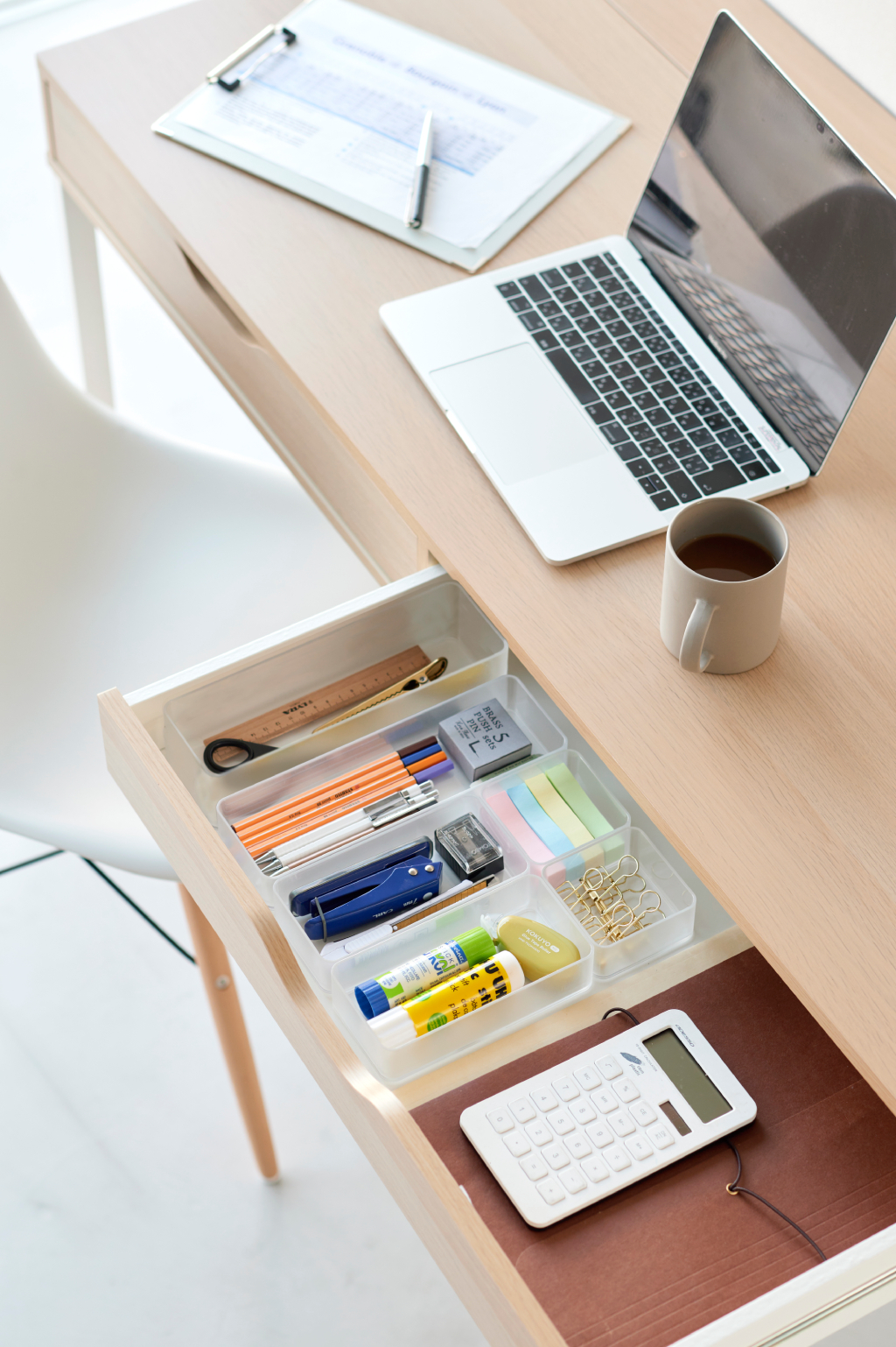 Scrivania con cassetto aperto pieno di cancelleria. Laptop, tazza e documenti sulla scrivania.
