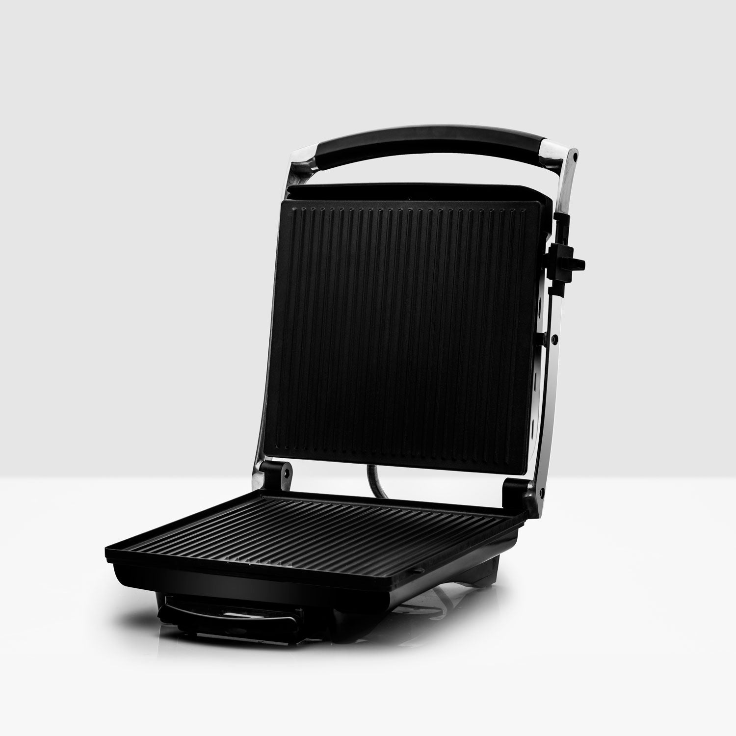 Een open zwarte panini grill met geribbelde grillplaten staat op een witte ondergrond.