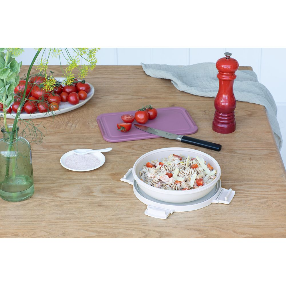 Insalata di pasta in una ciotola con pomodori, macinapepe rosso ed erbe aromatiche.