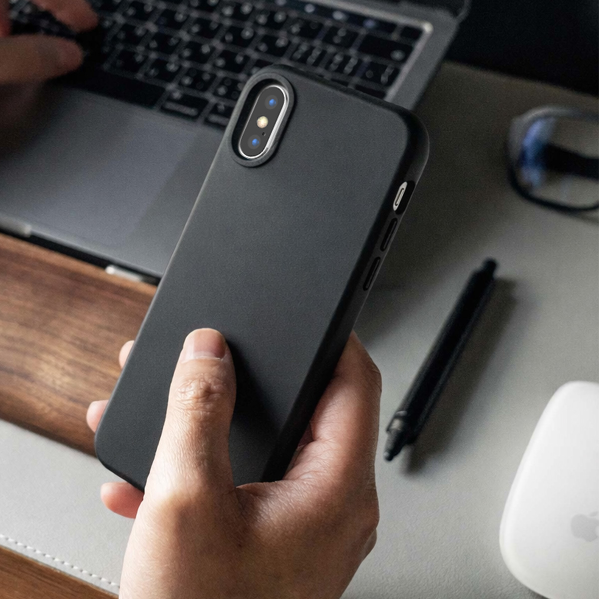 Une personne tient un smartphone noir avec un étui noir devant un ordinateur portable.