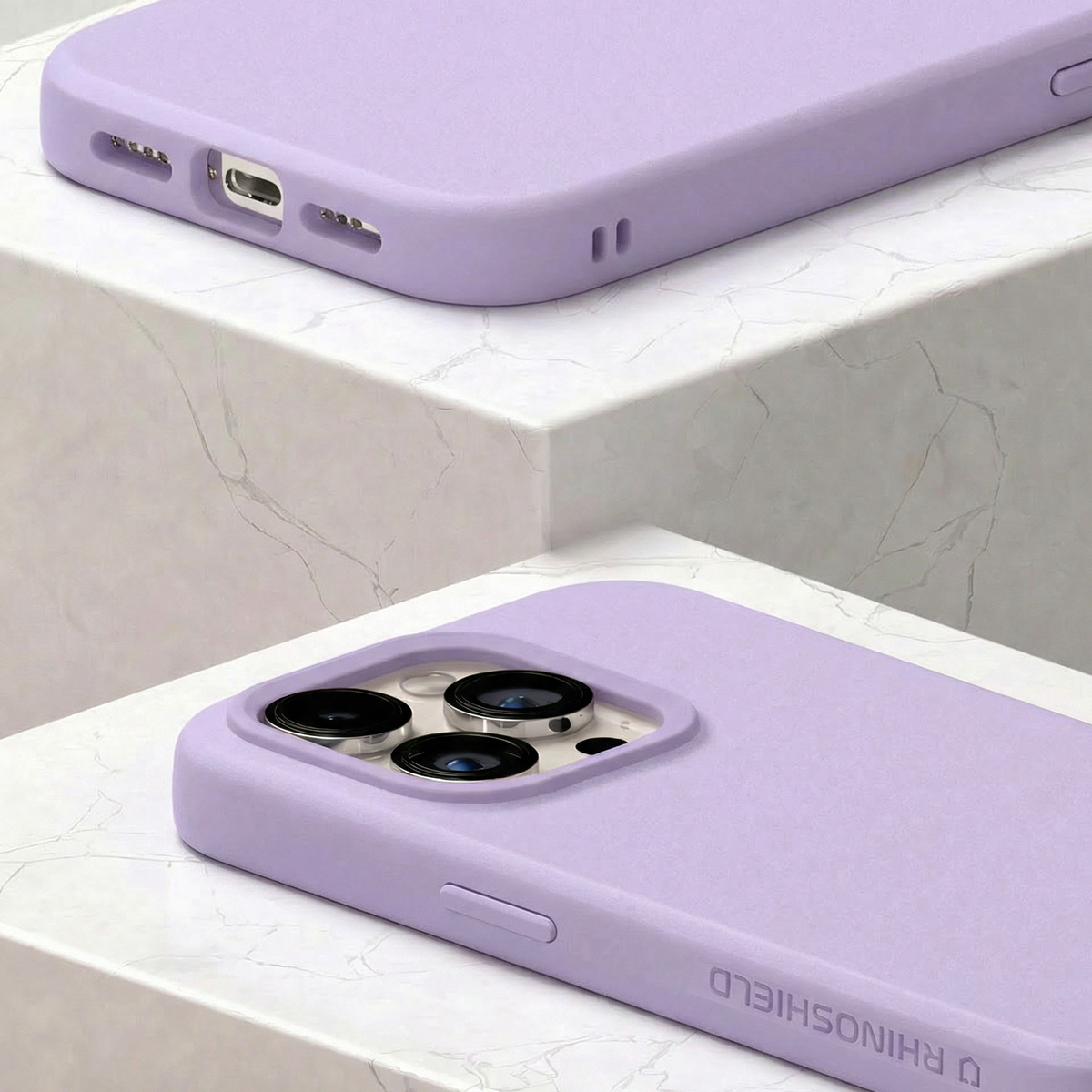 Deux coques iPhone lavande sur marbre. L'une montre les caméras, l'autre le port de charge.