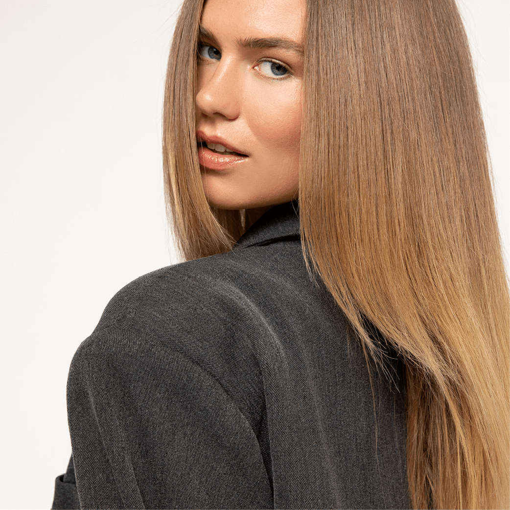 Woman with blonde hair in a dark gray blazer looks over her shoulder.