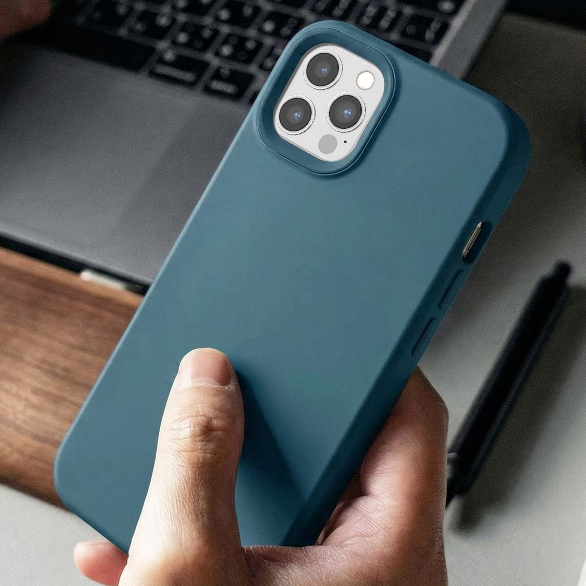 Main tenant une coque de téléphone bleu sarcelle avec objectif triple appareil photo sur un ordinateur portable.