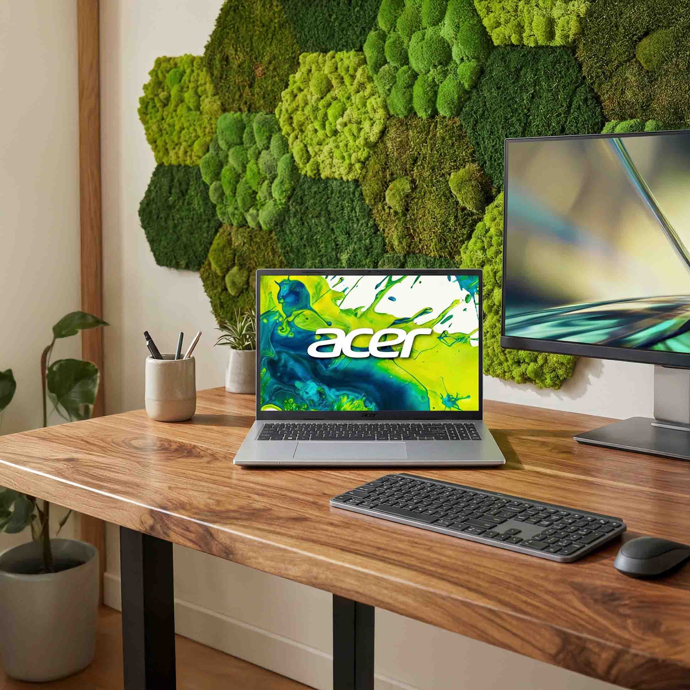 Ein Laptop und Monitor auf einem Holztisch vor einer Mooswand.