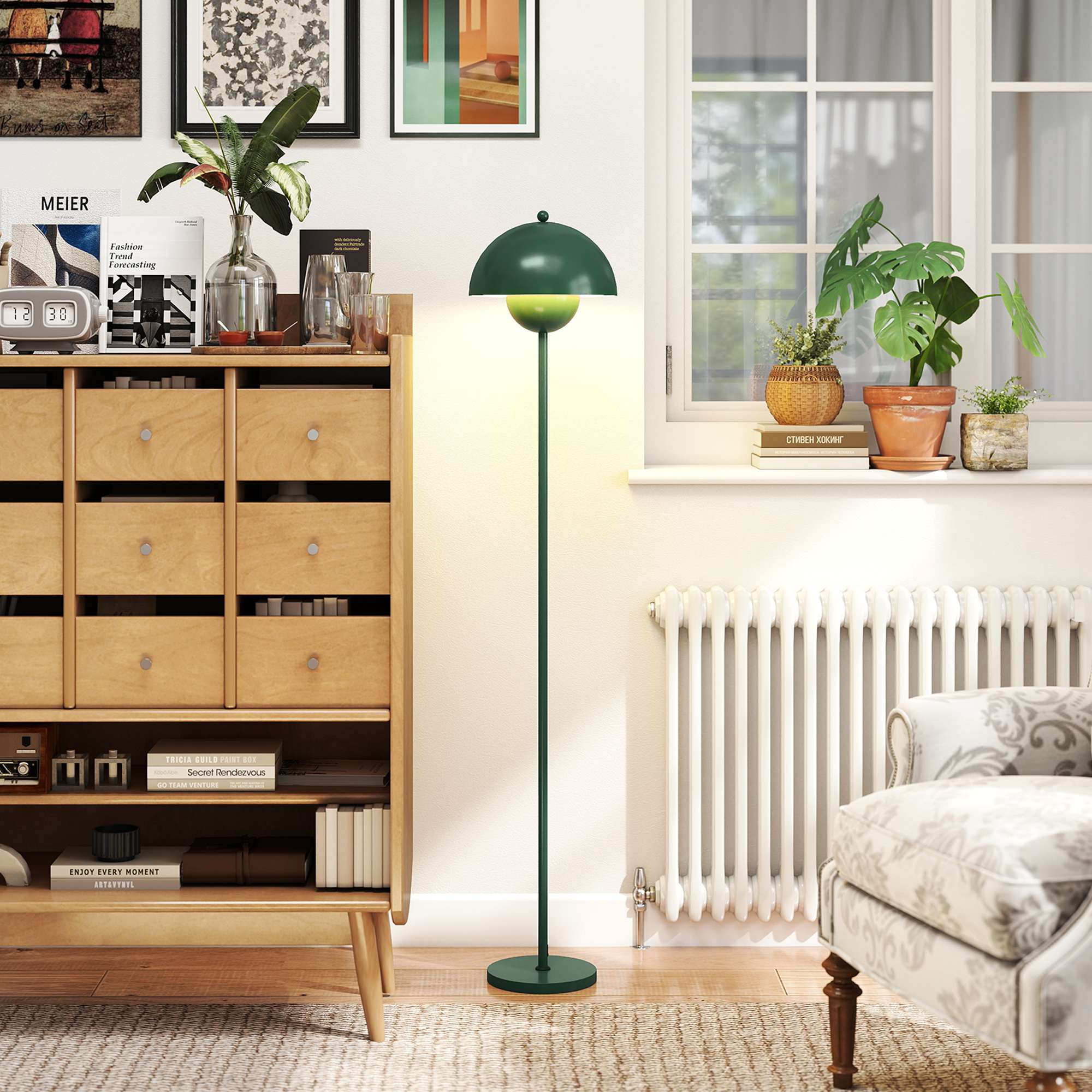 Una lampada da terra verde accanto a una cassettiera in legno con libri e piante.