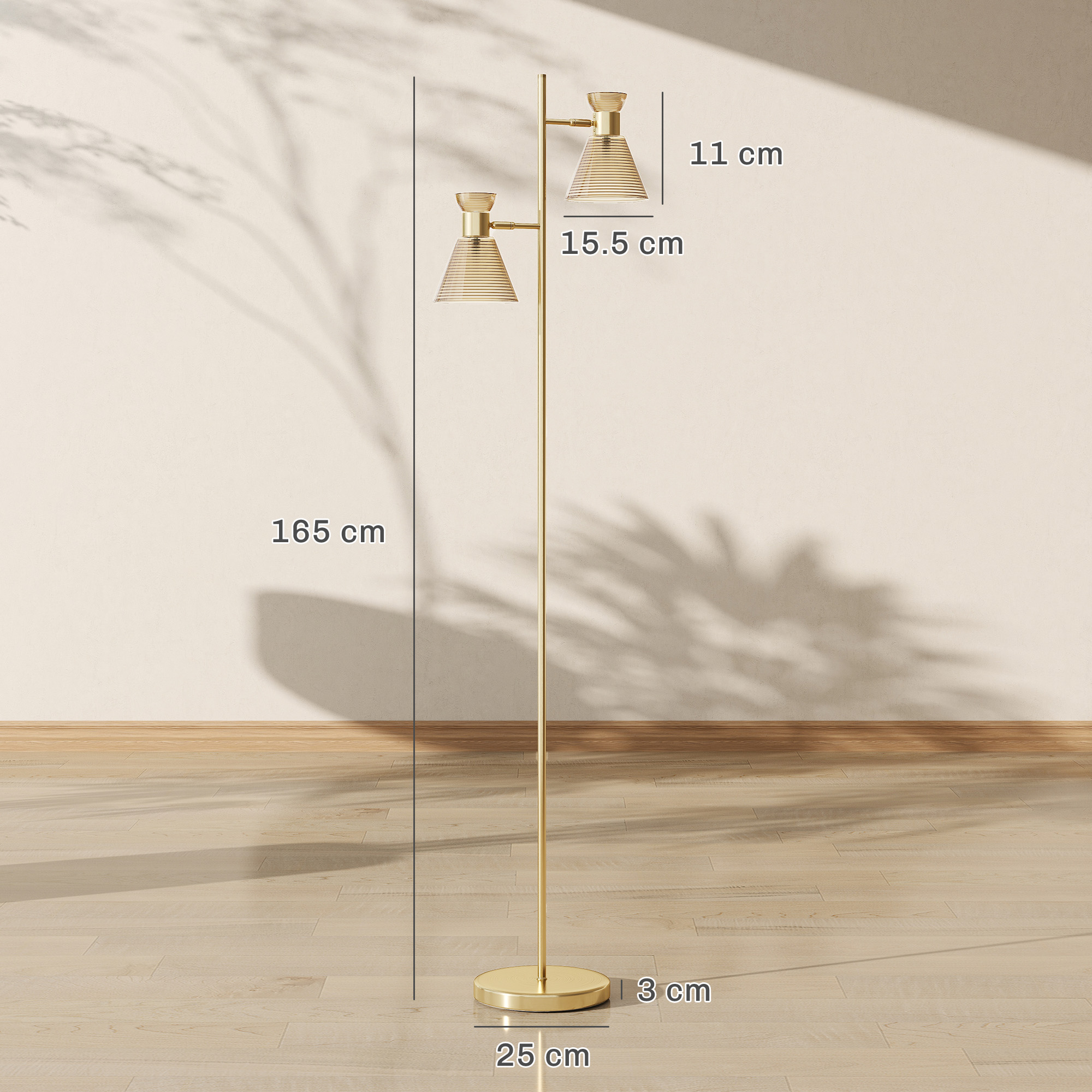 Lampada da terra dorata con due paralumi su parquet chiaro davanti a parete color crema.