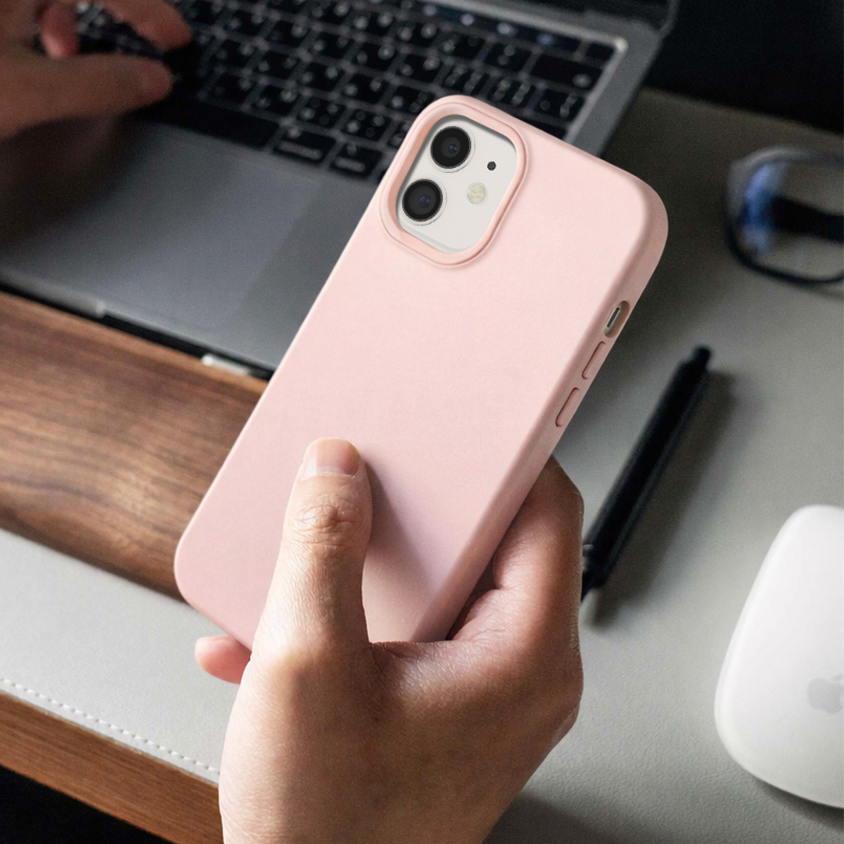 Een hand houdt een roze iPhone met camera's vast voor een laptop en muis.