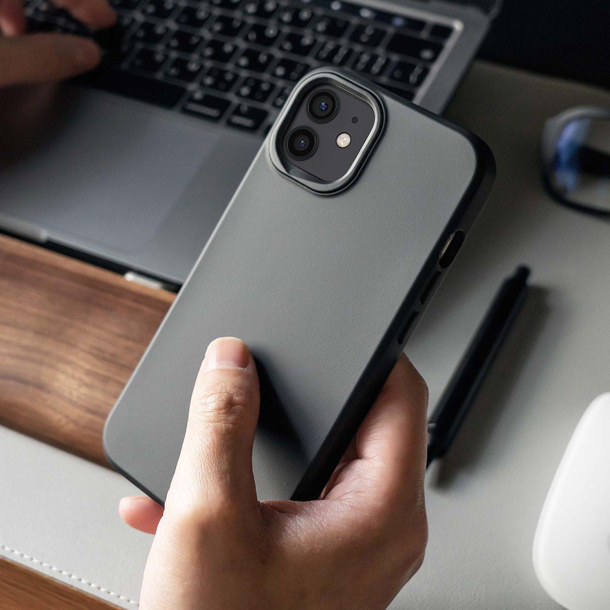 Een hand houdt een grijze smartphone vast voor een laptop. Een pen en muis liggen ernaast.
