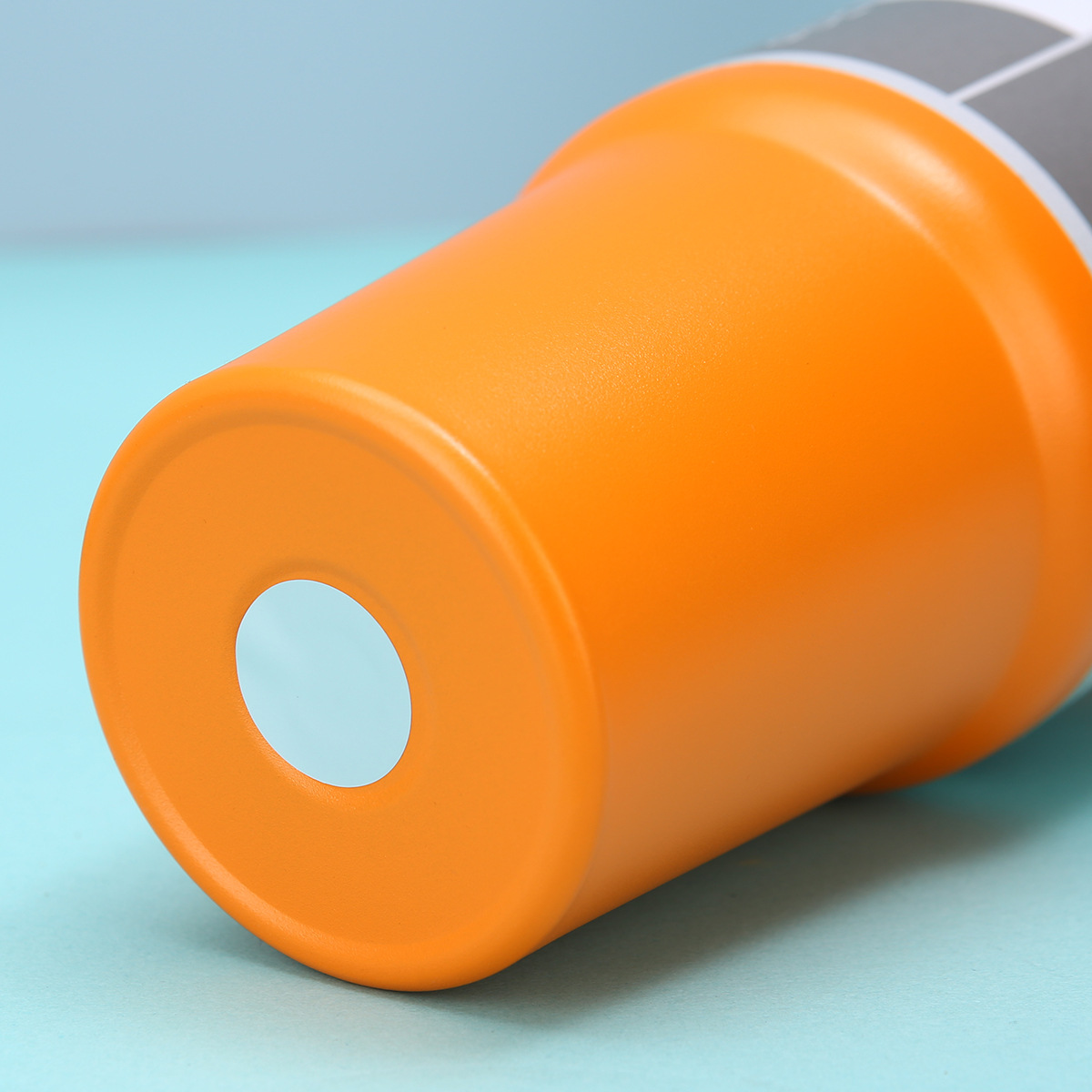 Orangefarbener Becher mit weißem Punkt liegt auf blauem Hintergrund.
