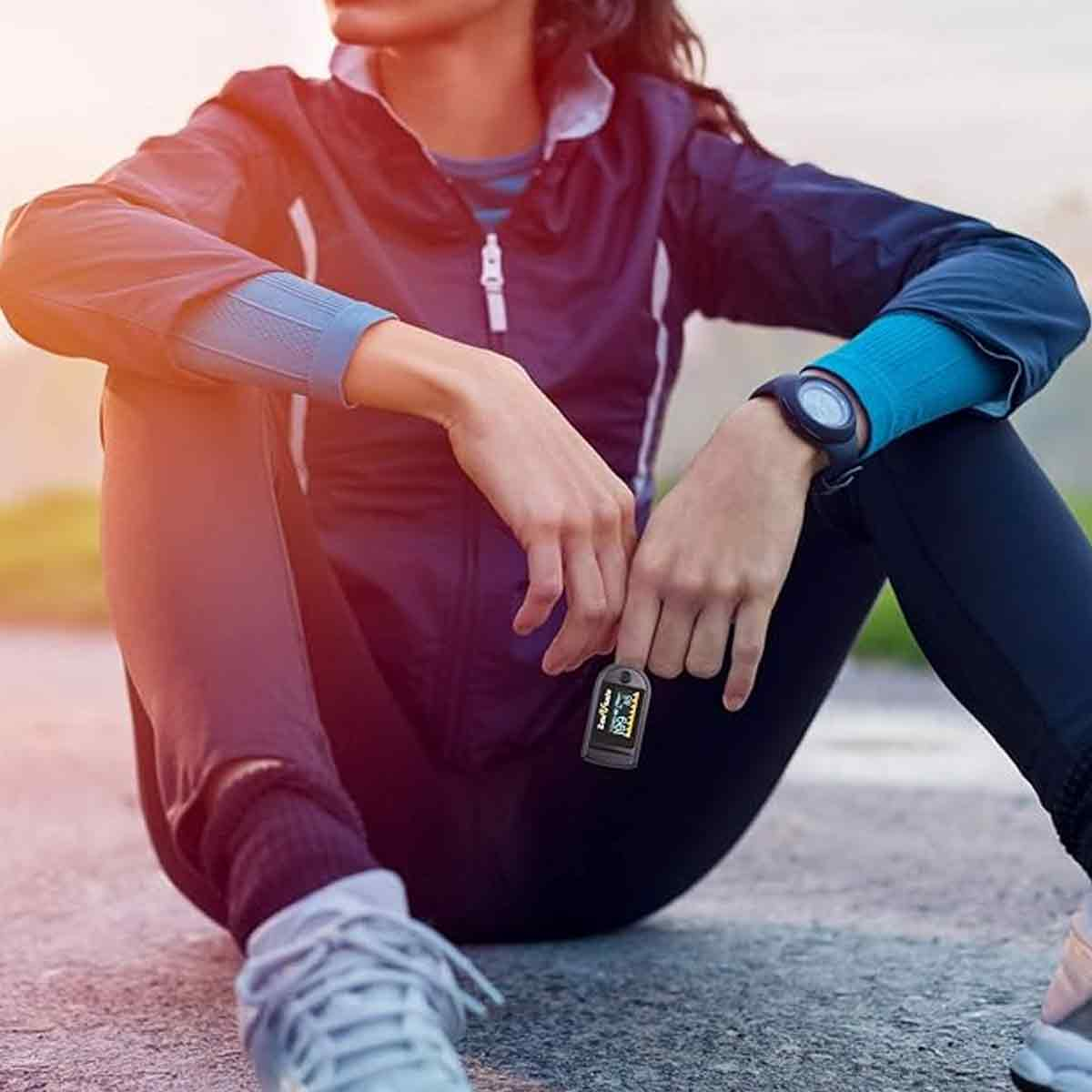 Eine Person in Sportkleidung sitzt auf dem Boden und hält ein Pulsoximeter.