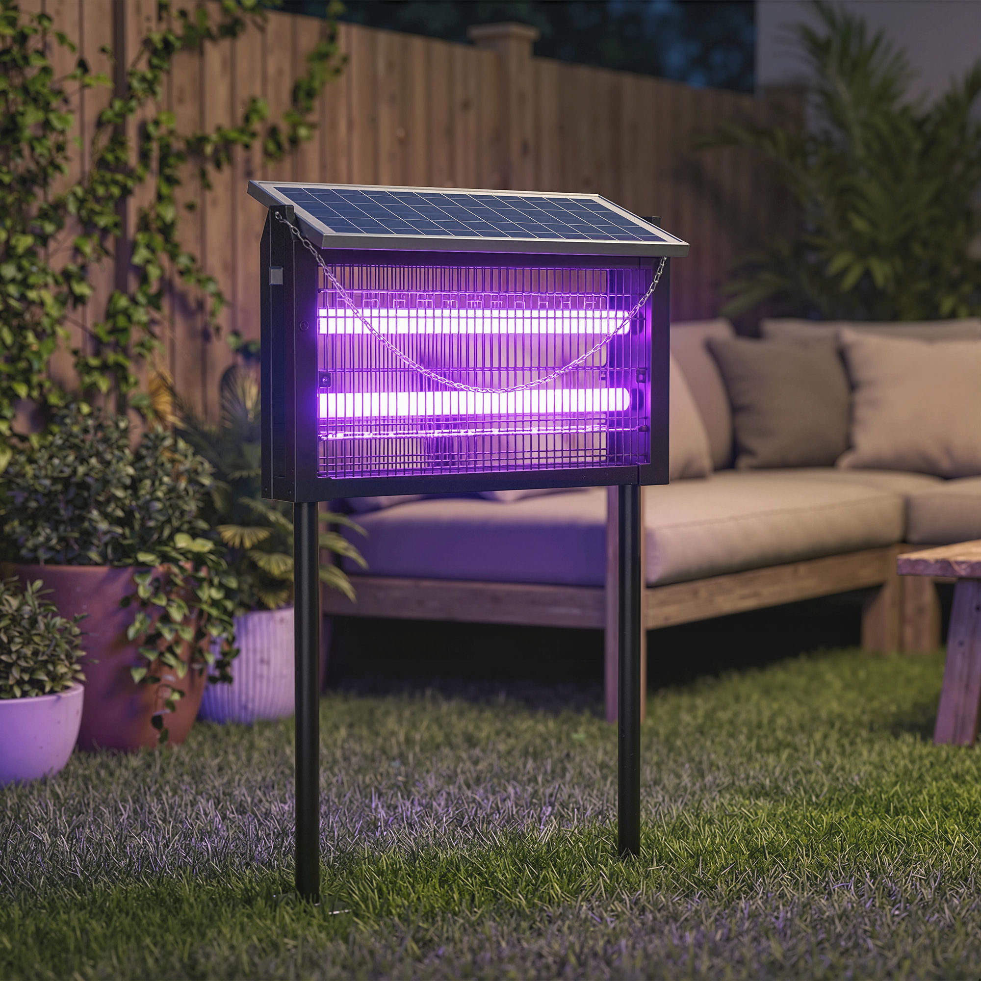 Dispositivo antizanzare solare con luce viola su prato vicino a piante e mobili da esterno.
