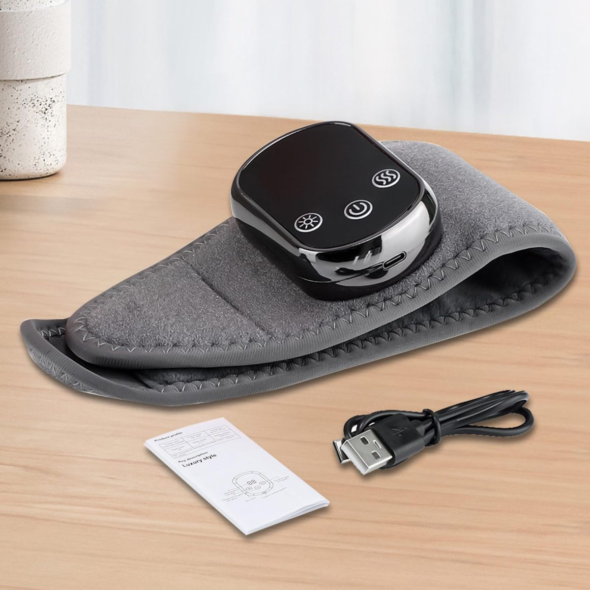 Ein schwarzes Steuergerät mit Symbolen liegt auf einem grauen Band. Ein USB-Kabel und eine Anleitung liegen daneben.