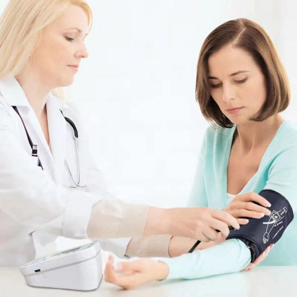 Ärztin misst Blutdruck bei Patientin mit Manschette und Gerät.