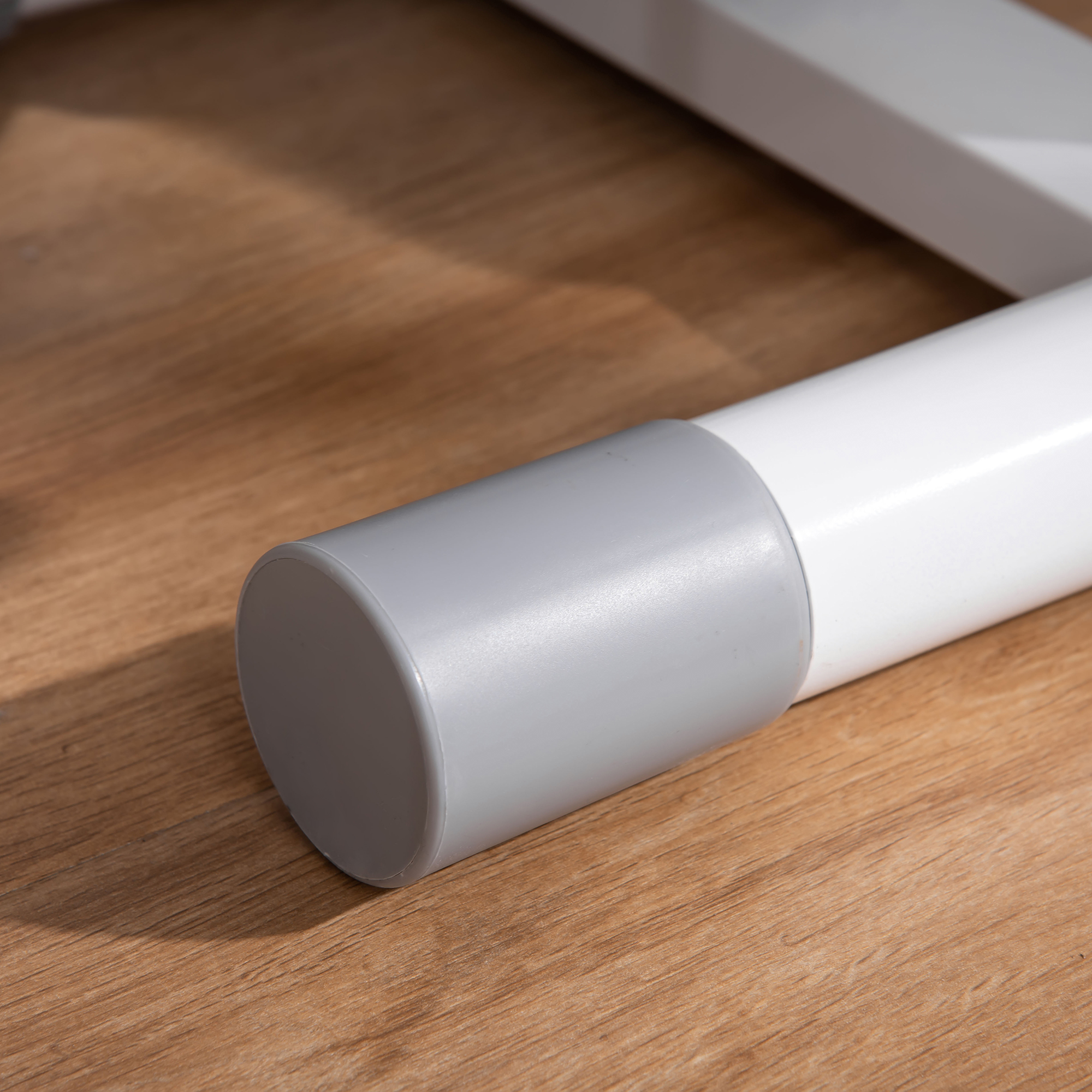 Un tubo bianco con un'estremità a cappuccio grigio su un pavimento in legno.