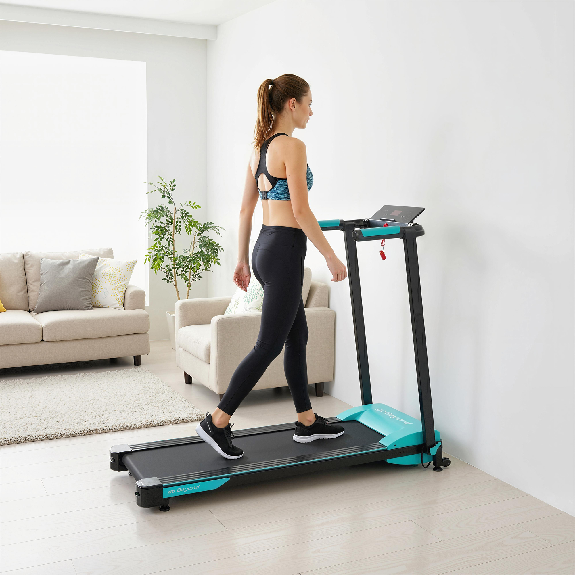 Una donna in abiti sportivi cammina su un tapis roulant blu in un soggiorno.