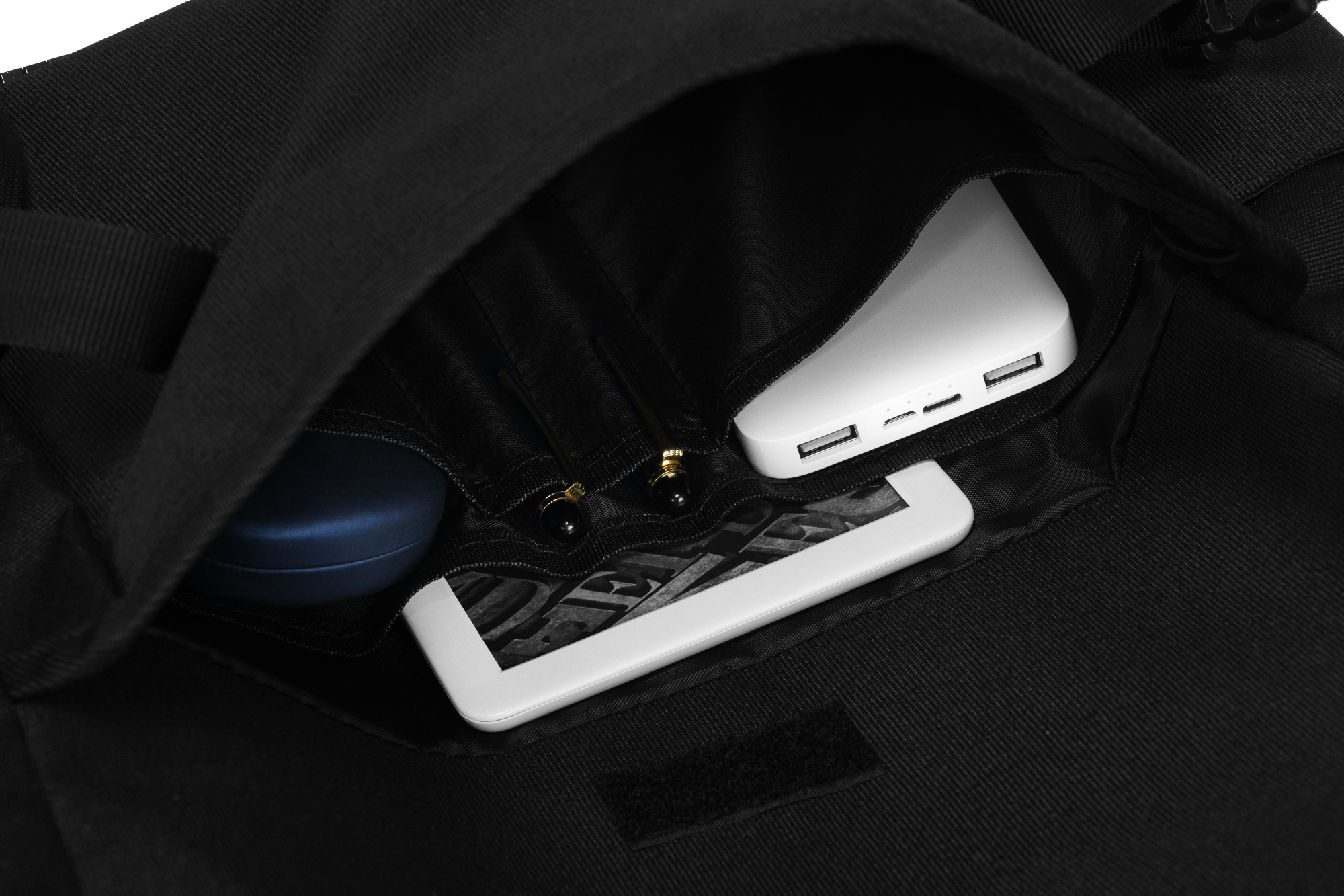 Wewnątrz czarnej torby: biały power bank, tablet i niebieskie etui. Zorganizowane przechowywanie.