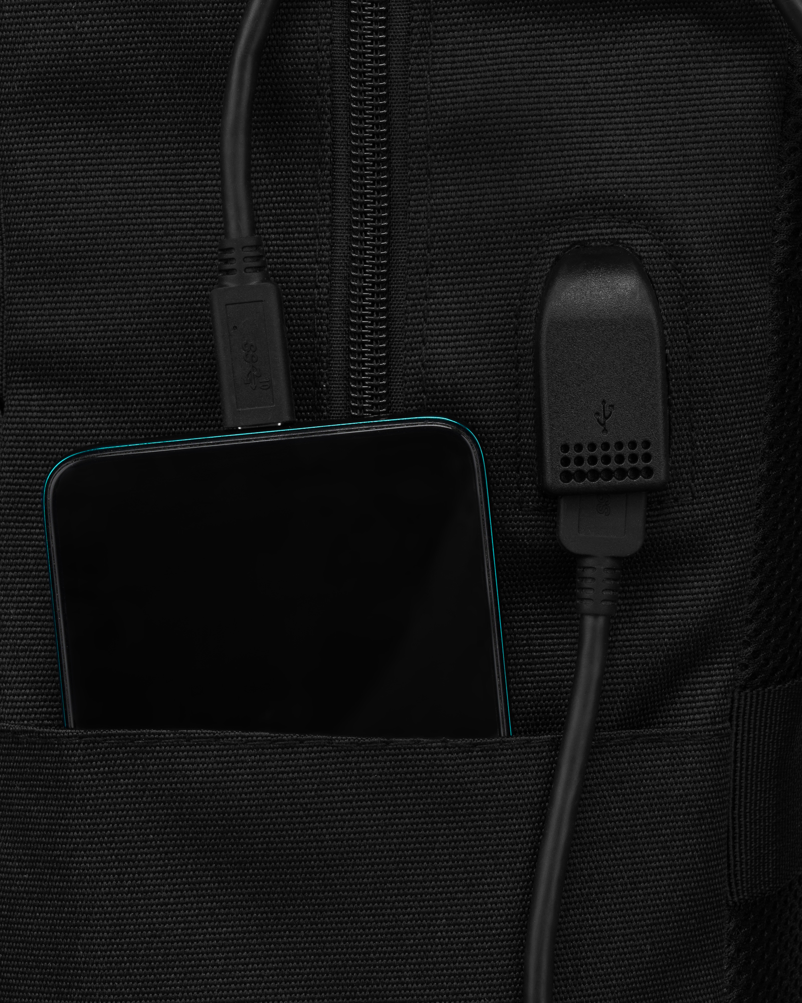 Czarny smartfon ładuje się przez kabel USB w kieszeni czarnej torby.