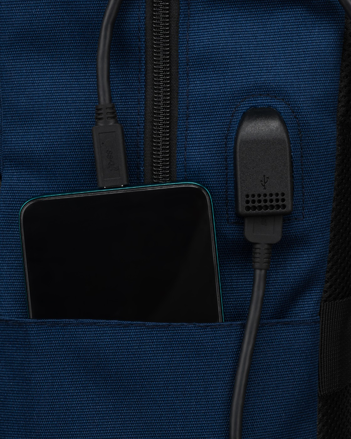 Smartfon ładuje się w niebieskiej torbie, podłączony kablami USB.