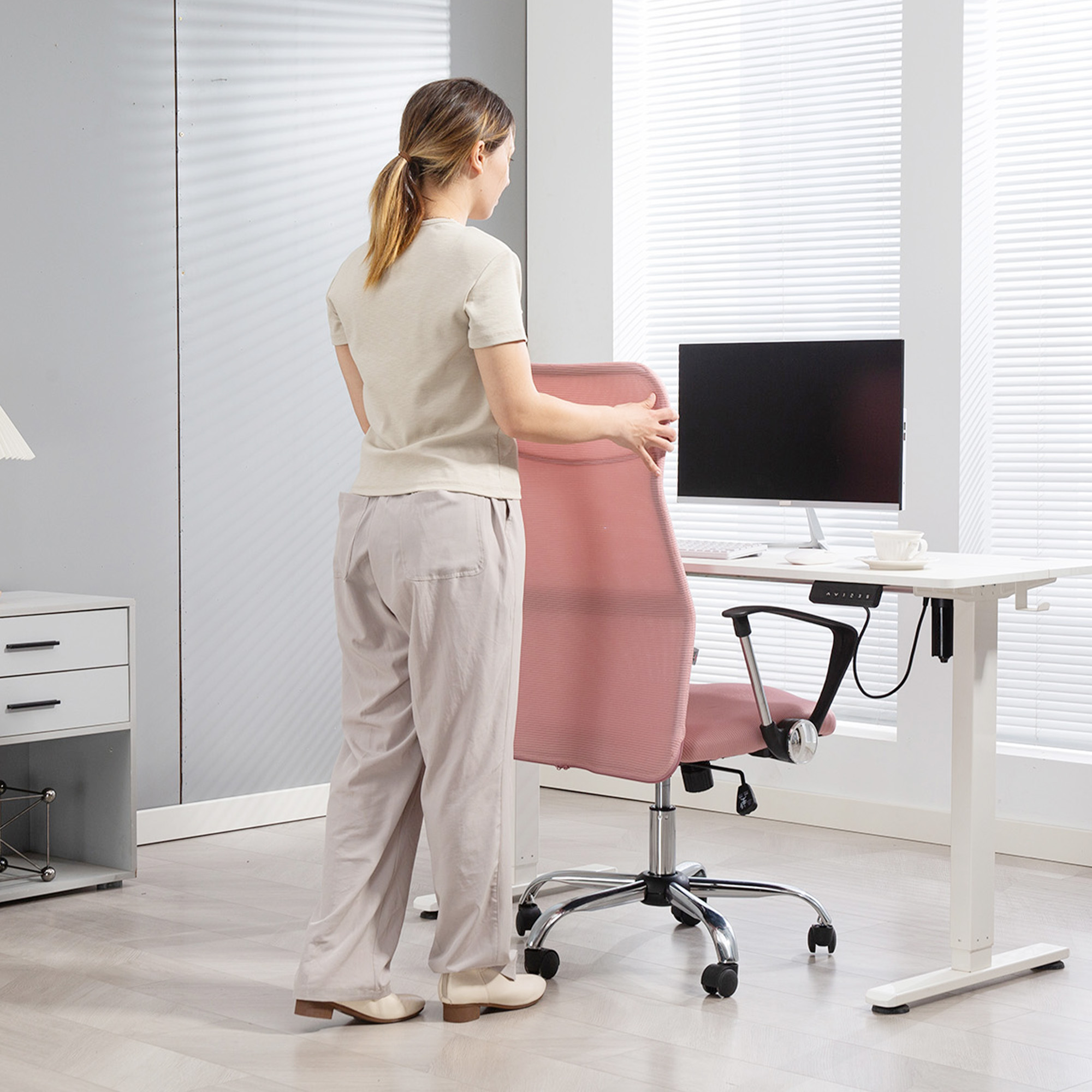 Una donna spinge una sedia da ufficio rosa verso una scrivania bianca con un monitor.