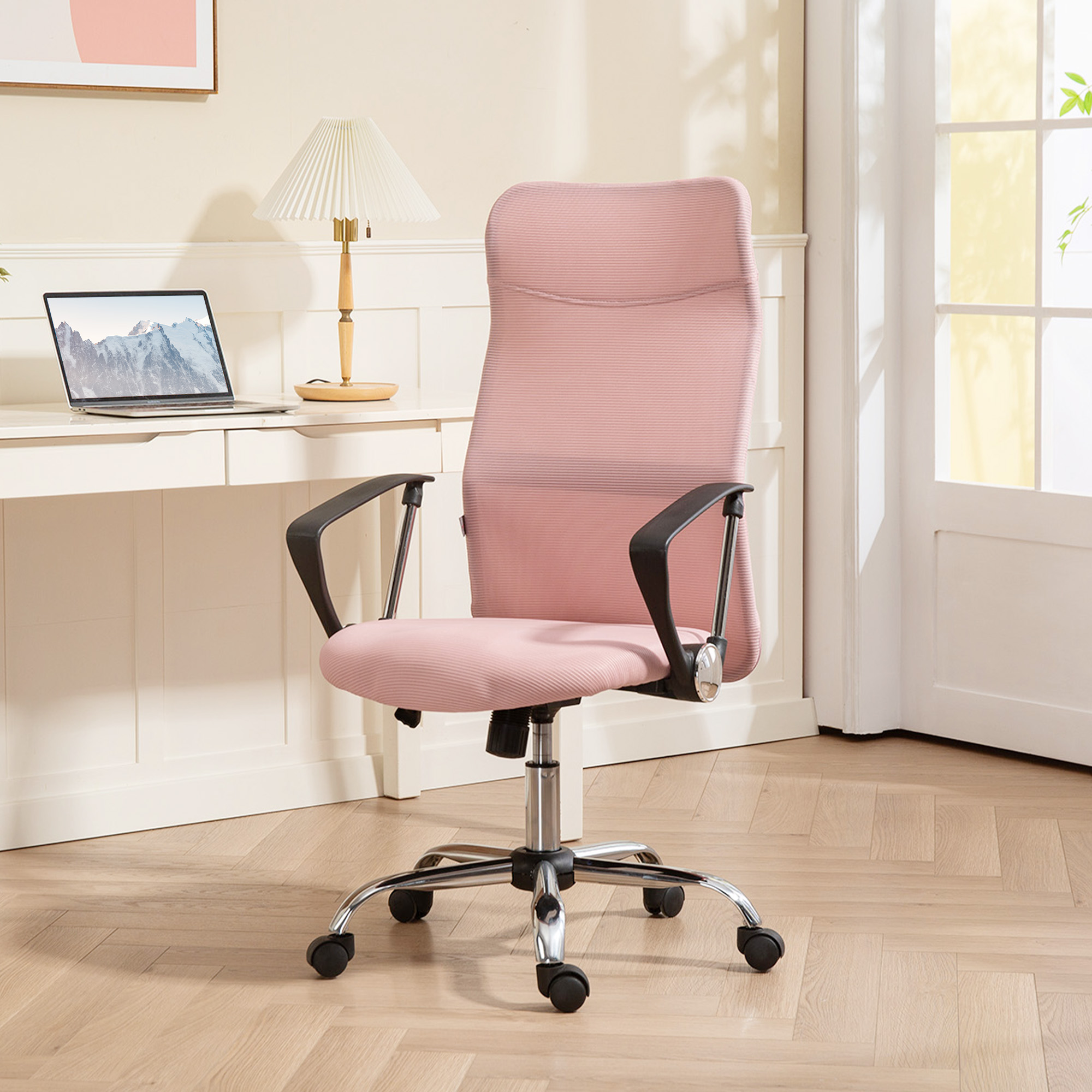 Una sedia da ufficio rosa con braccioli si trova su un pavimento in legno accanto a una scrivania con laptop e lampada.