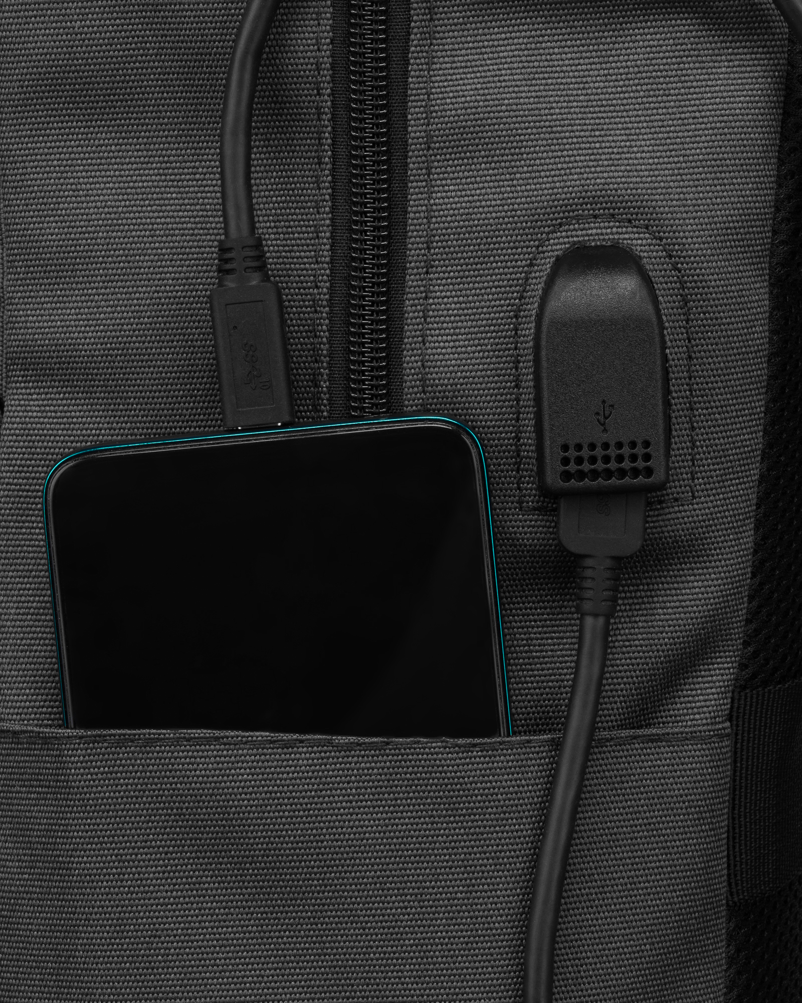 Smartfon znajduje się w kieszeni szarego plecaka, podłączony dwoma kablami USB.
