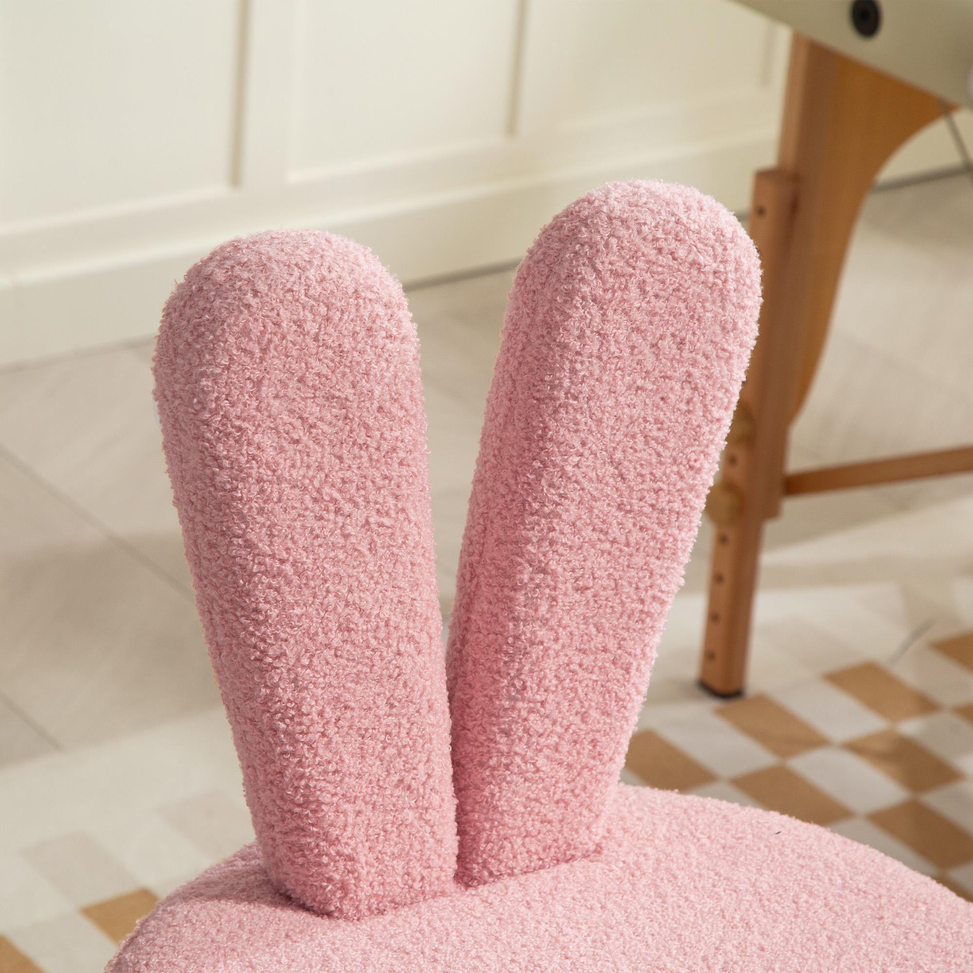 Una sedia rosa di peluche con orecchie da coniglio su un pavimento a scacchi.