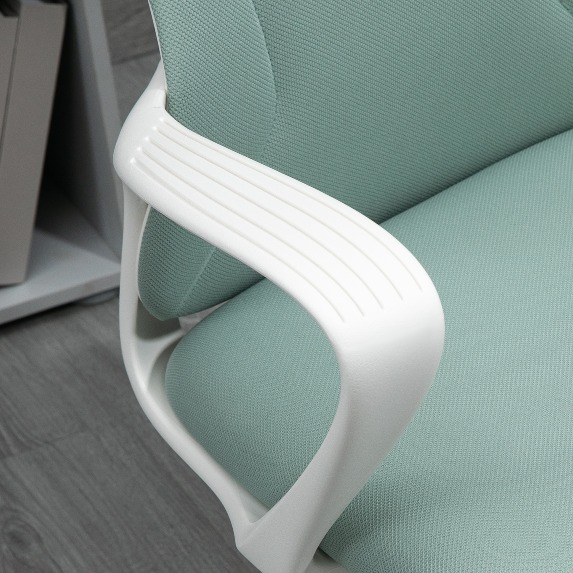 Sedia in tessuto verde con dettaglio bracciolo bianco su pavimento in legno.