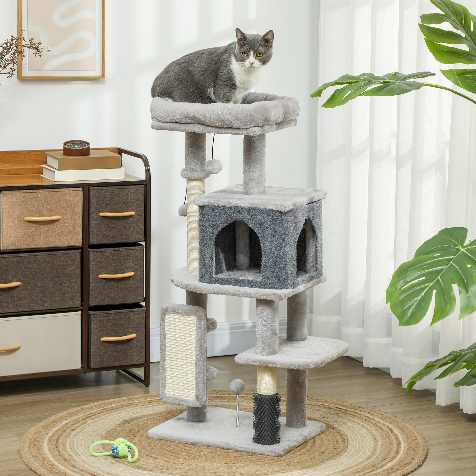 Un gatto seduto su un tiragraffi accanto a un mobiletto e una pianta.