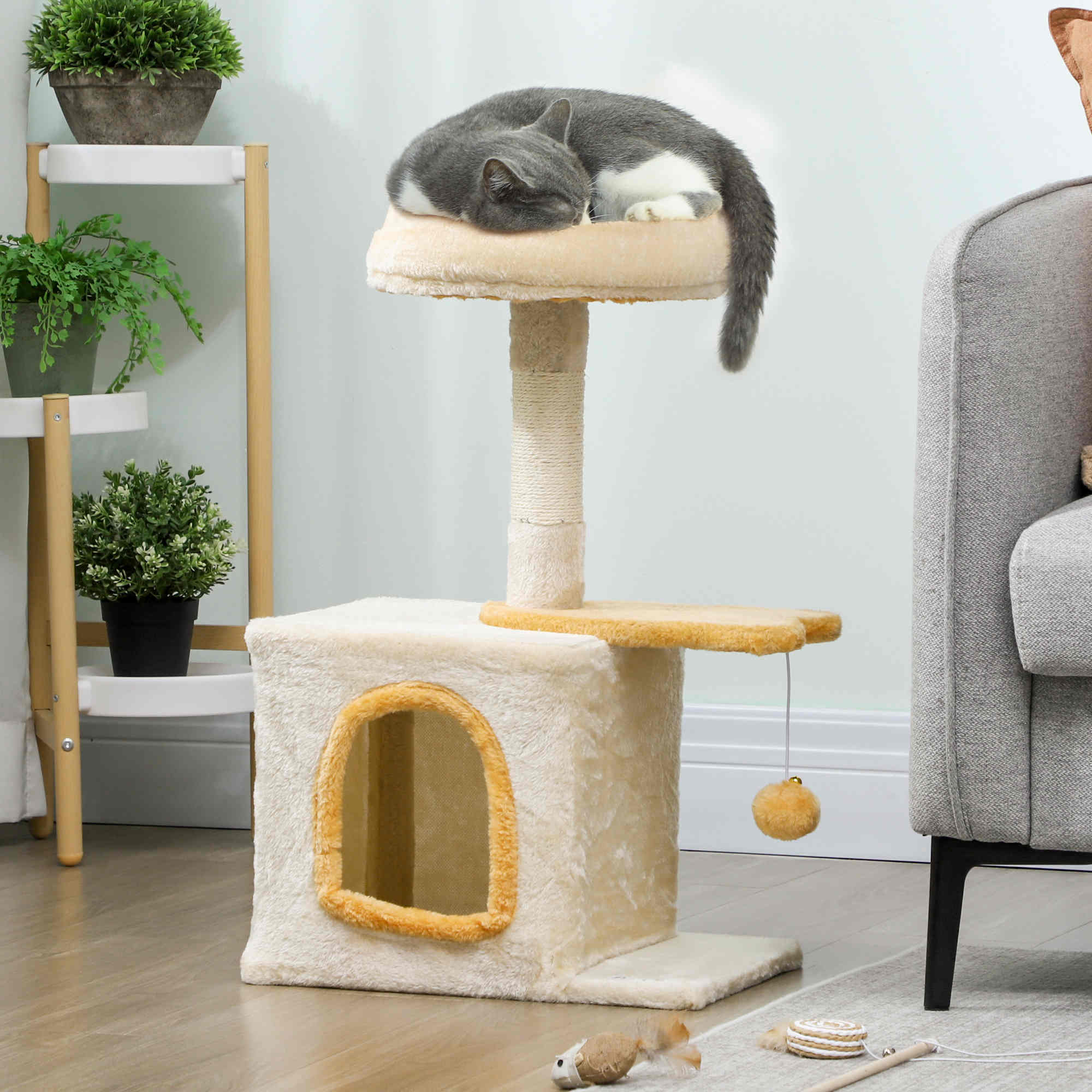 Gatto grigio e bianco dorme su un tiragraffi con giocattoli e piante.