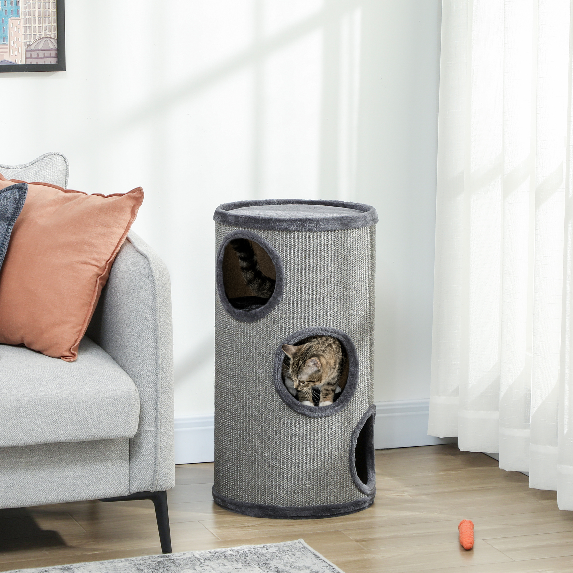 Un gatto tigrato sbircia da un tiragraffi a più livelli. Un divano grigio con cuscini è nelle vicinanze.