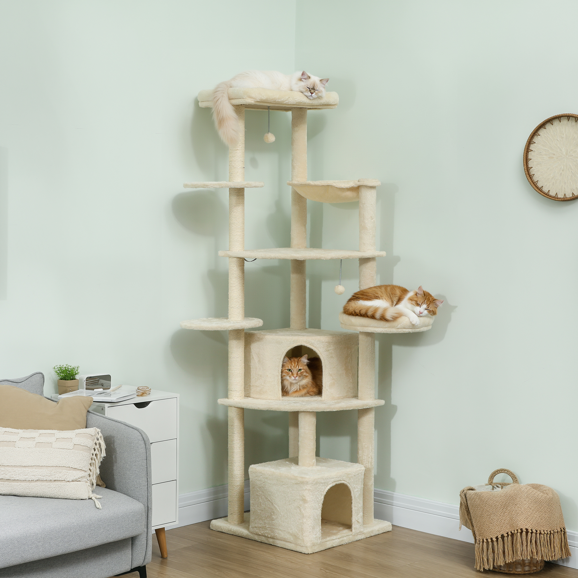 Tiragraffi a più livelli con tre gatti, parete verde chiaro, divano, cesto.