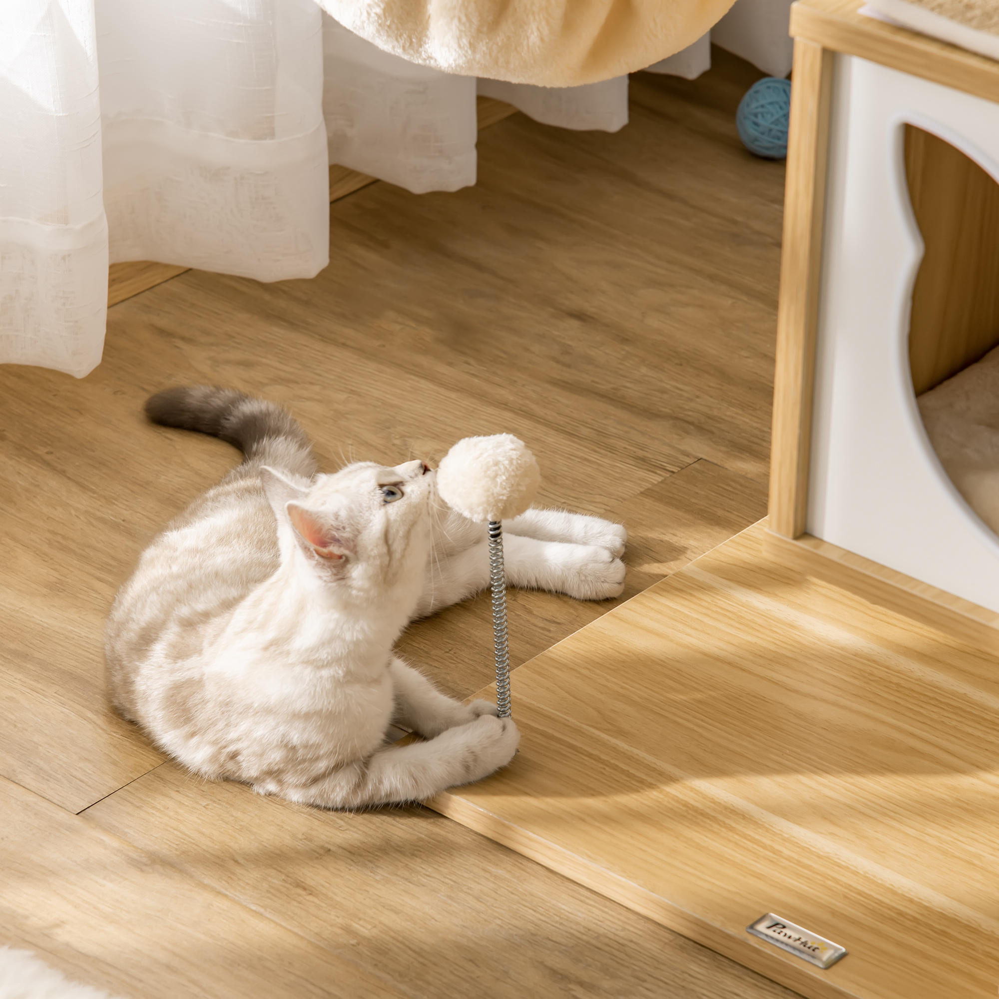 Un gatto gioca con un giocattolo sul pavimento di legno accanto a una casa per gatti.