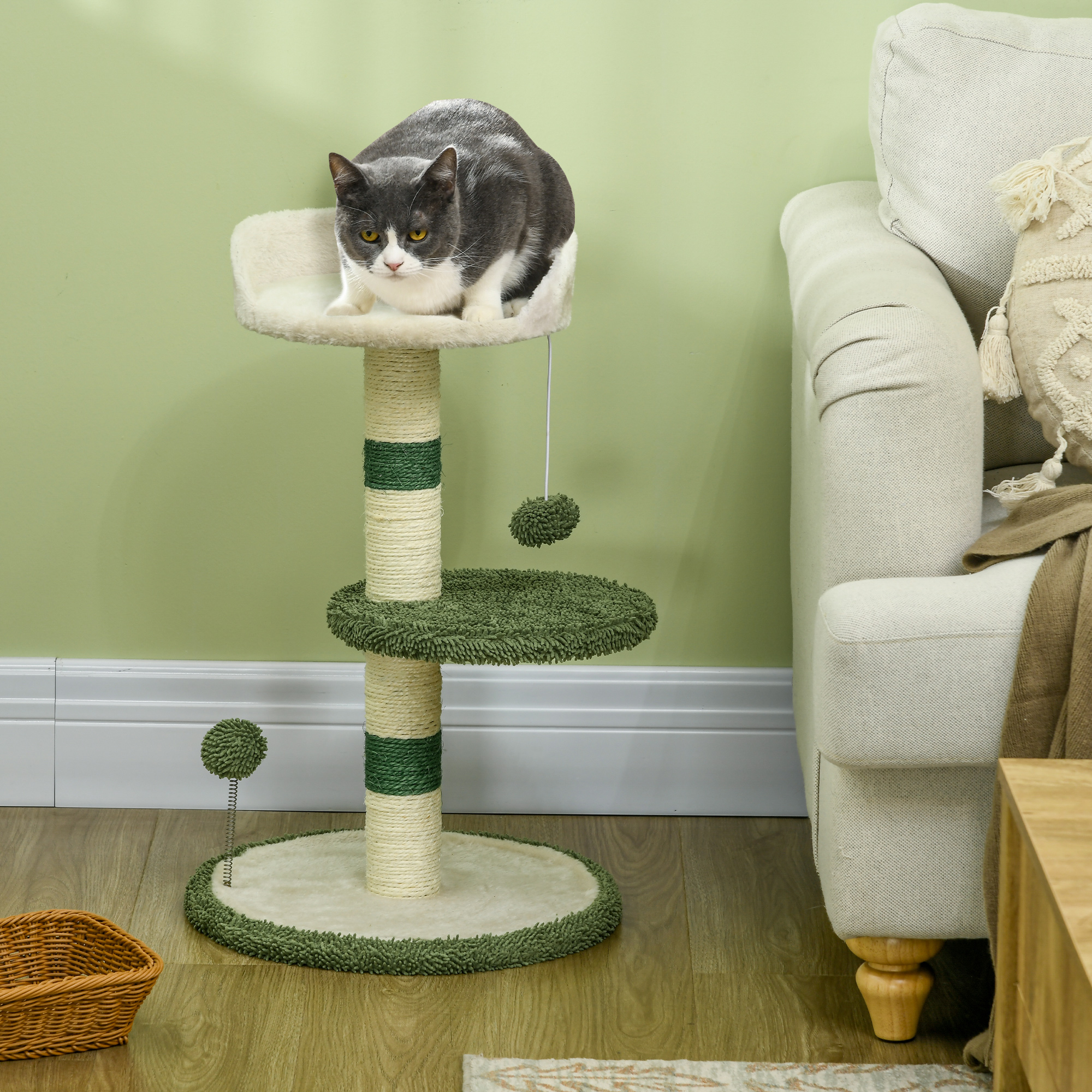 Un gatto grigio e bianco siede su una piattaforma di peluche di un albero per gatti. L'albero ha pali in sisal e piattaforme verdi.