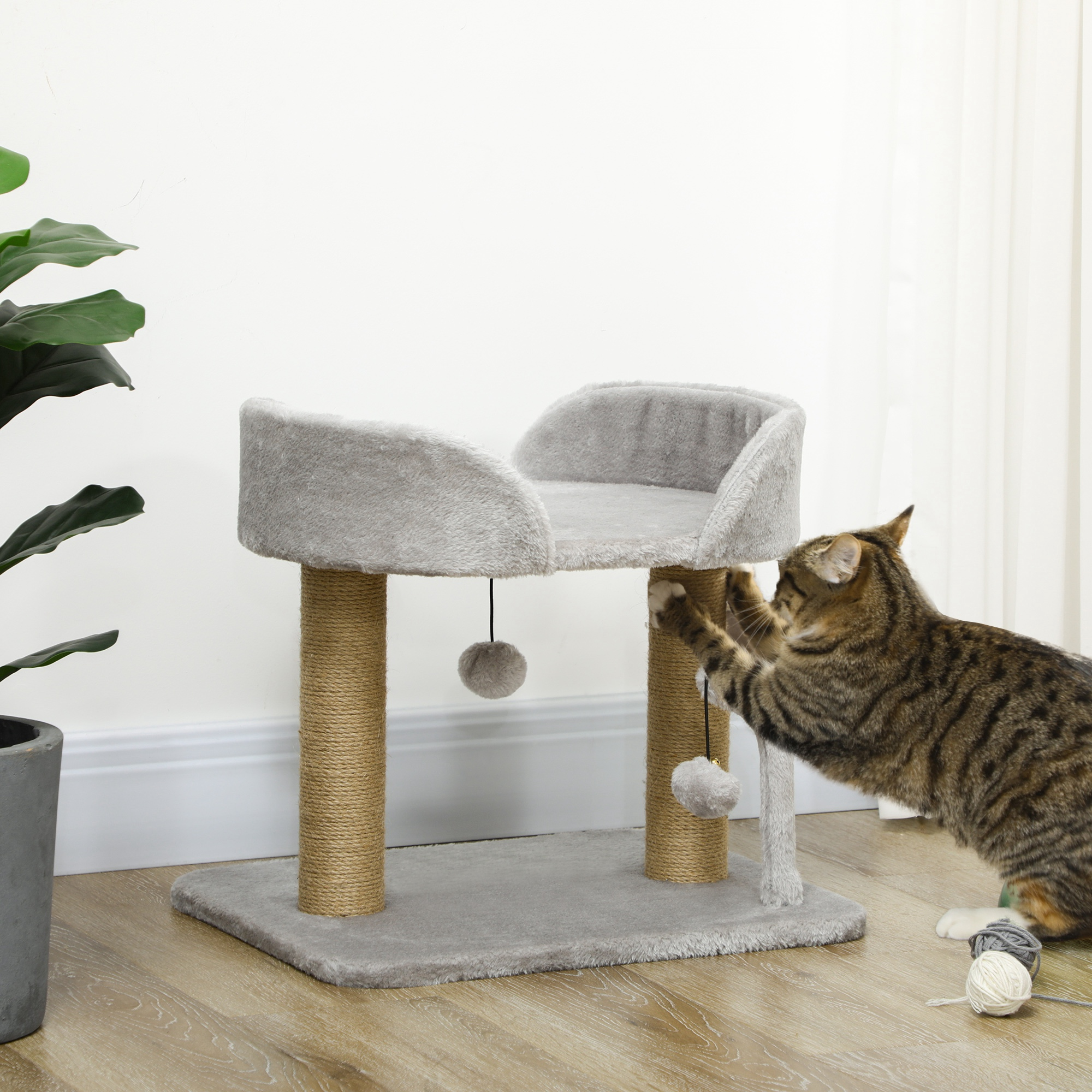 Un gatto tigrato gioca con un tiragraffi con palline e filato.
