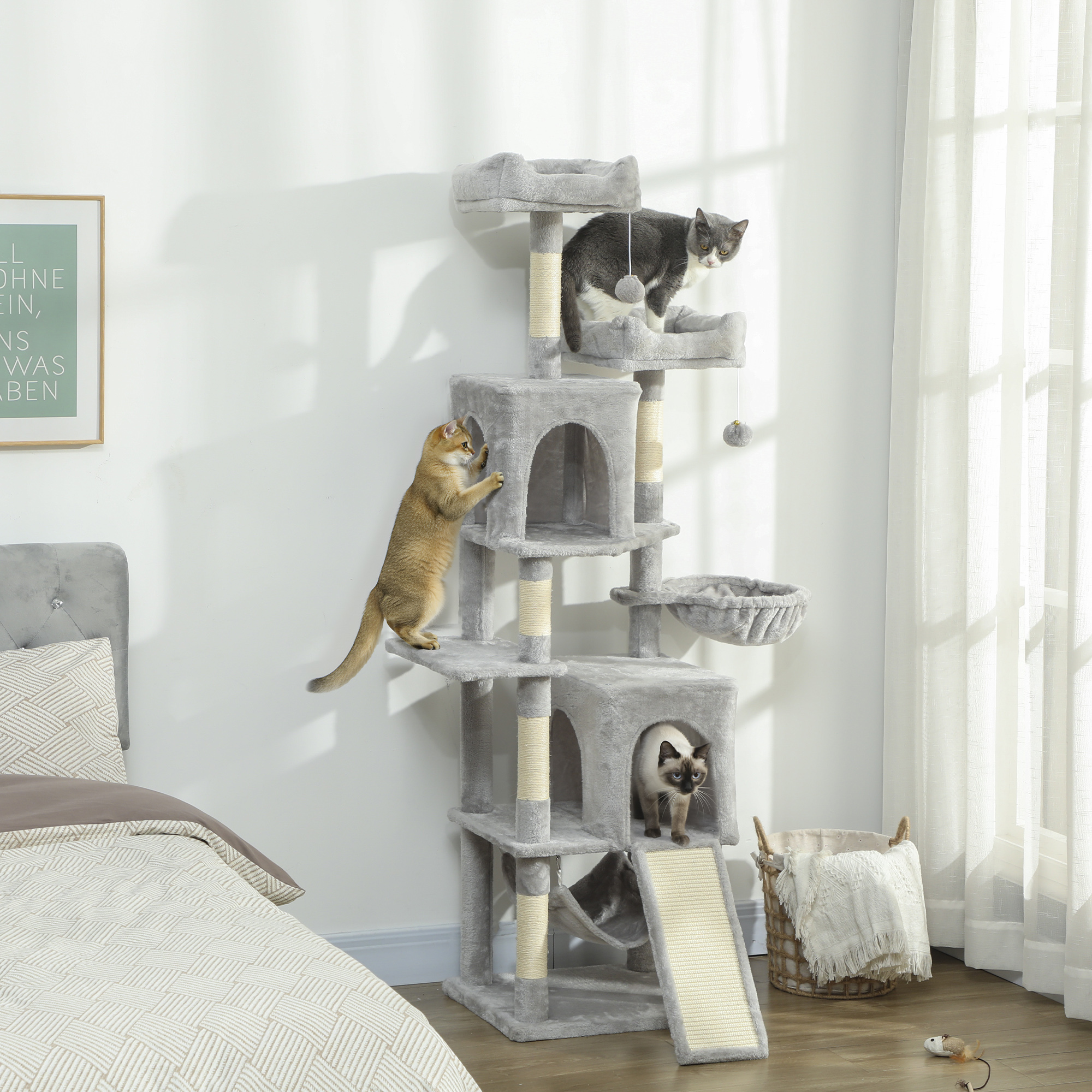 Tre gatti su un tiragraffi grigio in una camera da letto accanto a un letto.