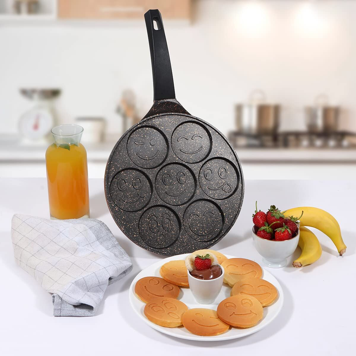 Padella per pancake con faccine sorridenti, servita con pancake, fragole, banana e succo.