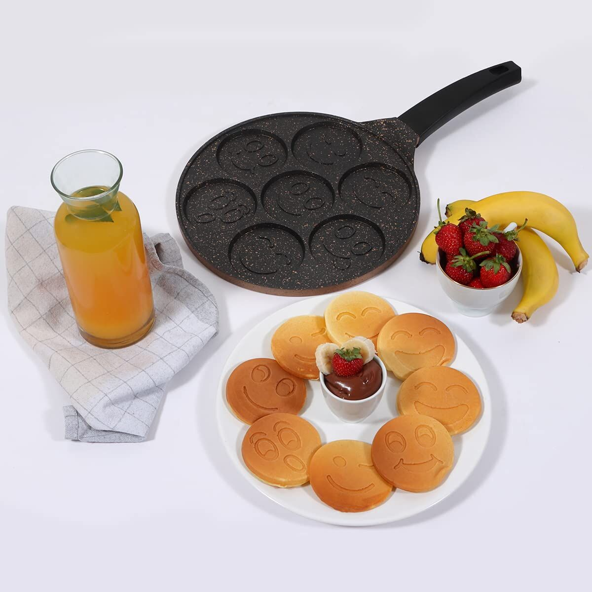Pancake a faccina sorridente su piatto con succo, fragole, banane e padella sorridente.