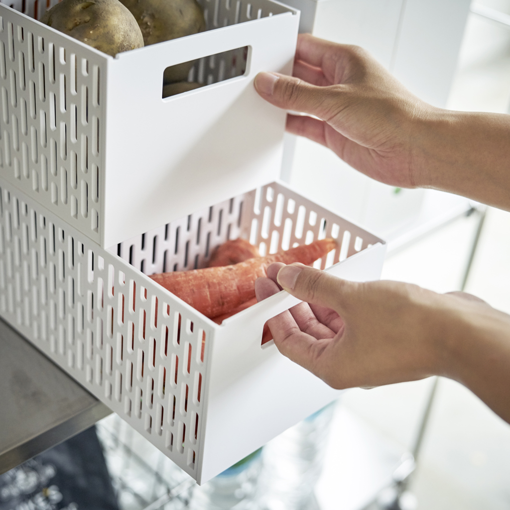 Mani che tirano un cassetto con carote da un'unità di stoccaggio bianca.